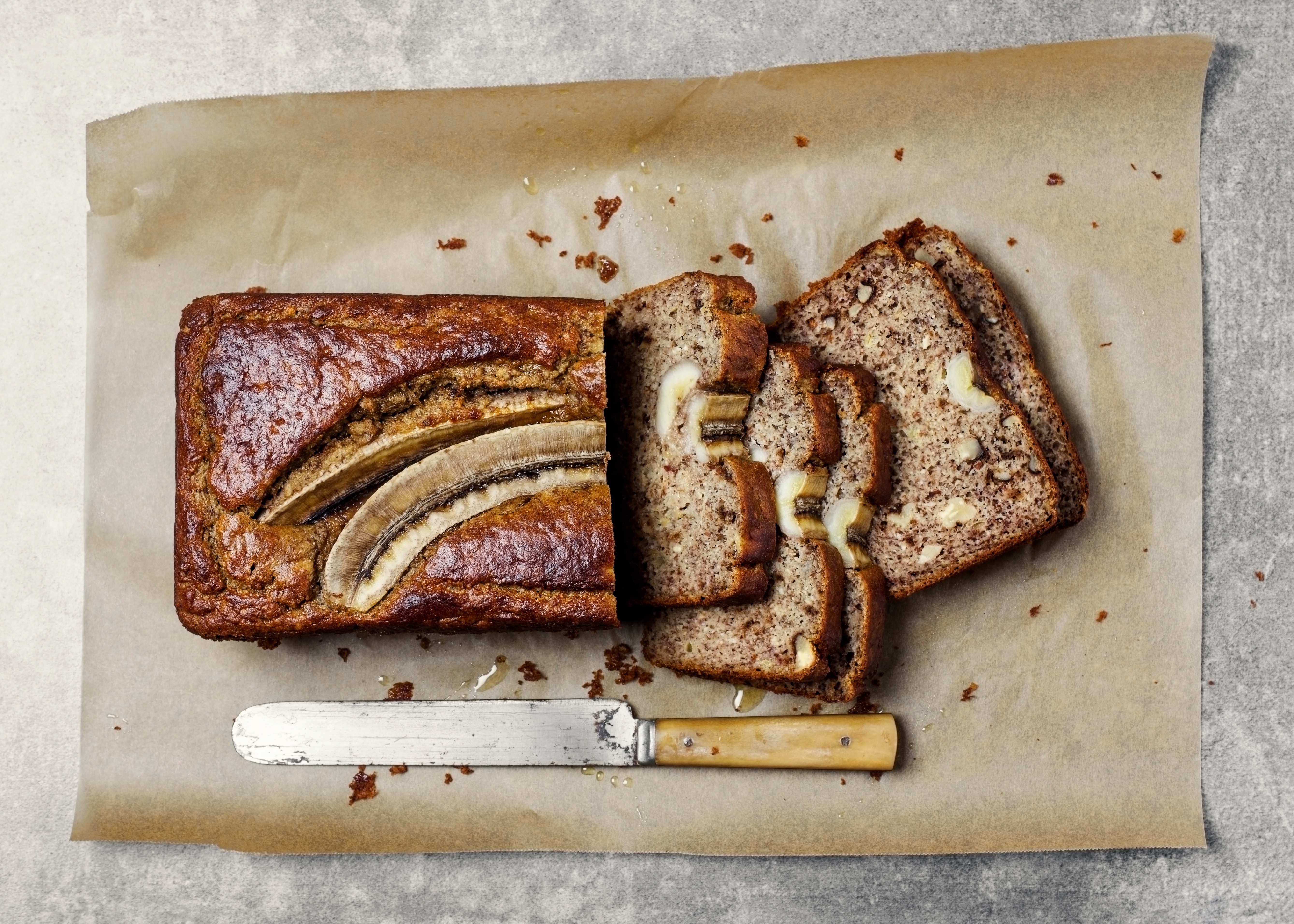 Sliced banana bread with a knife on parchment paper, showing a full banana baked into the top