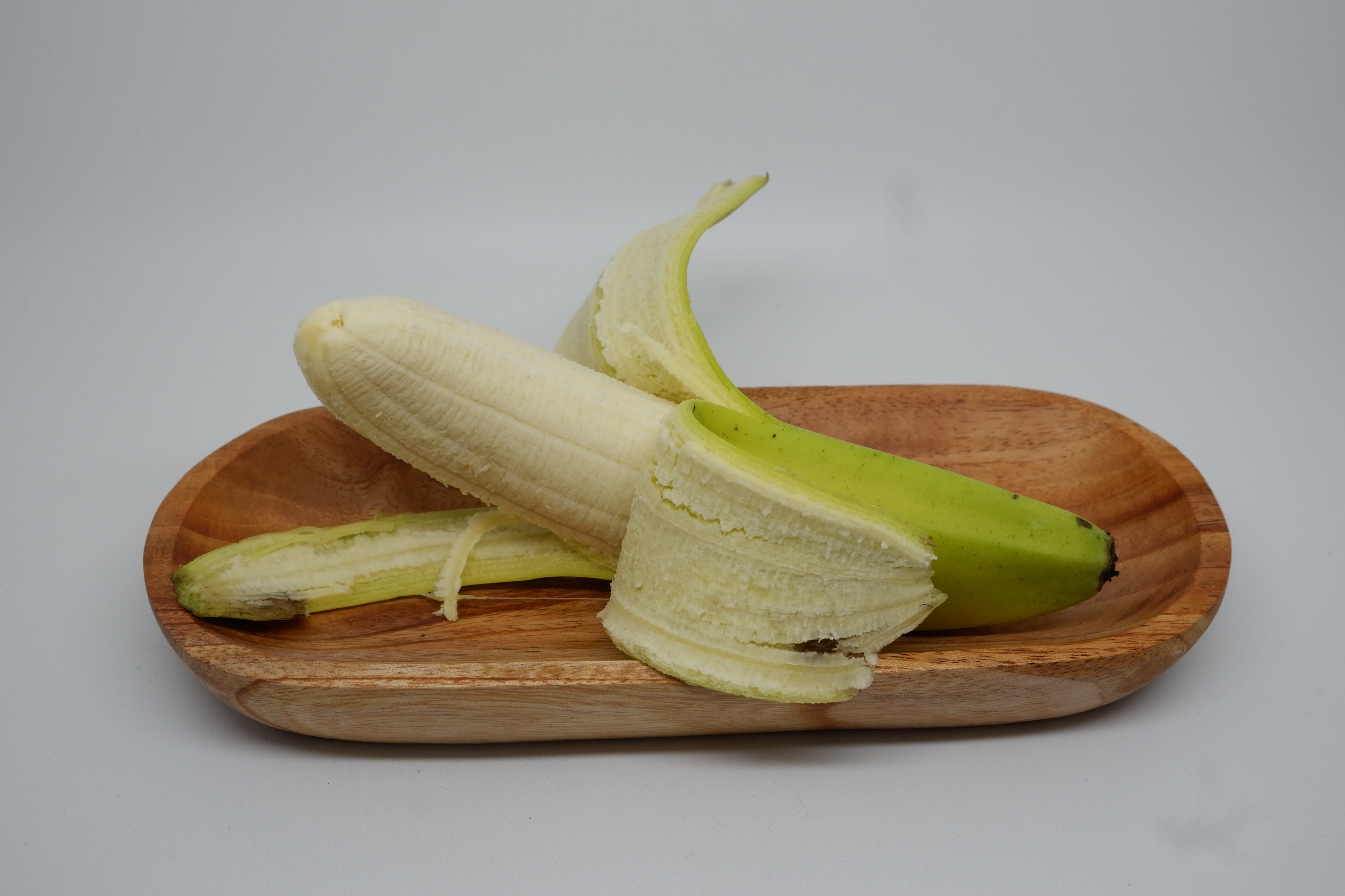 A peeled banana sits in a wooden tray on a plain background