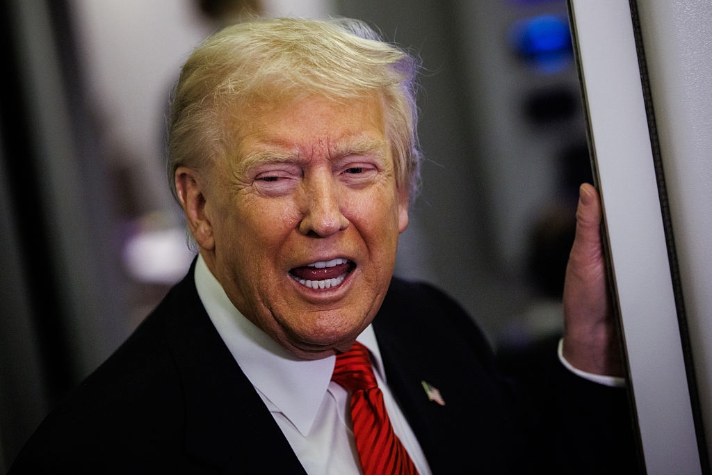 En person i en dress snakker, holder seg på en overflate for støtte, med en uttrykksfull ansiktsbevegelse