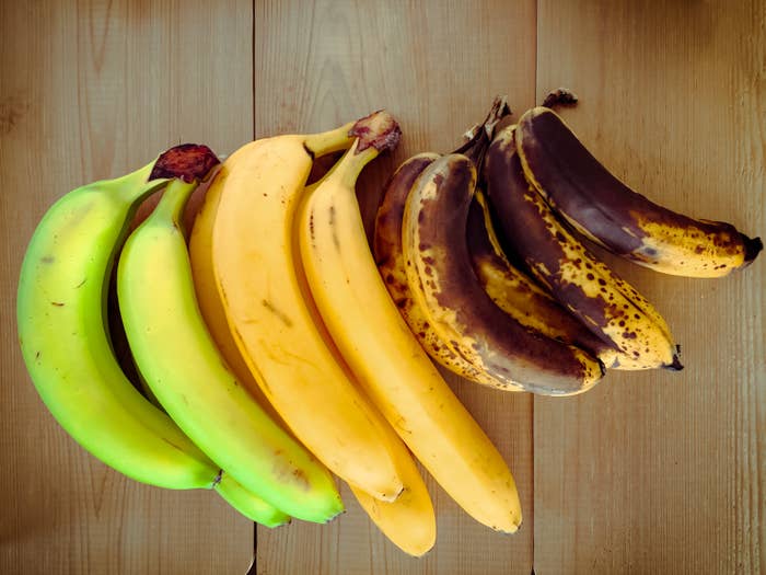 Bananas in various ripeness stages are lined up on a wooden surface, from green on the left to overripe on the right
