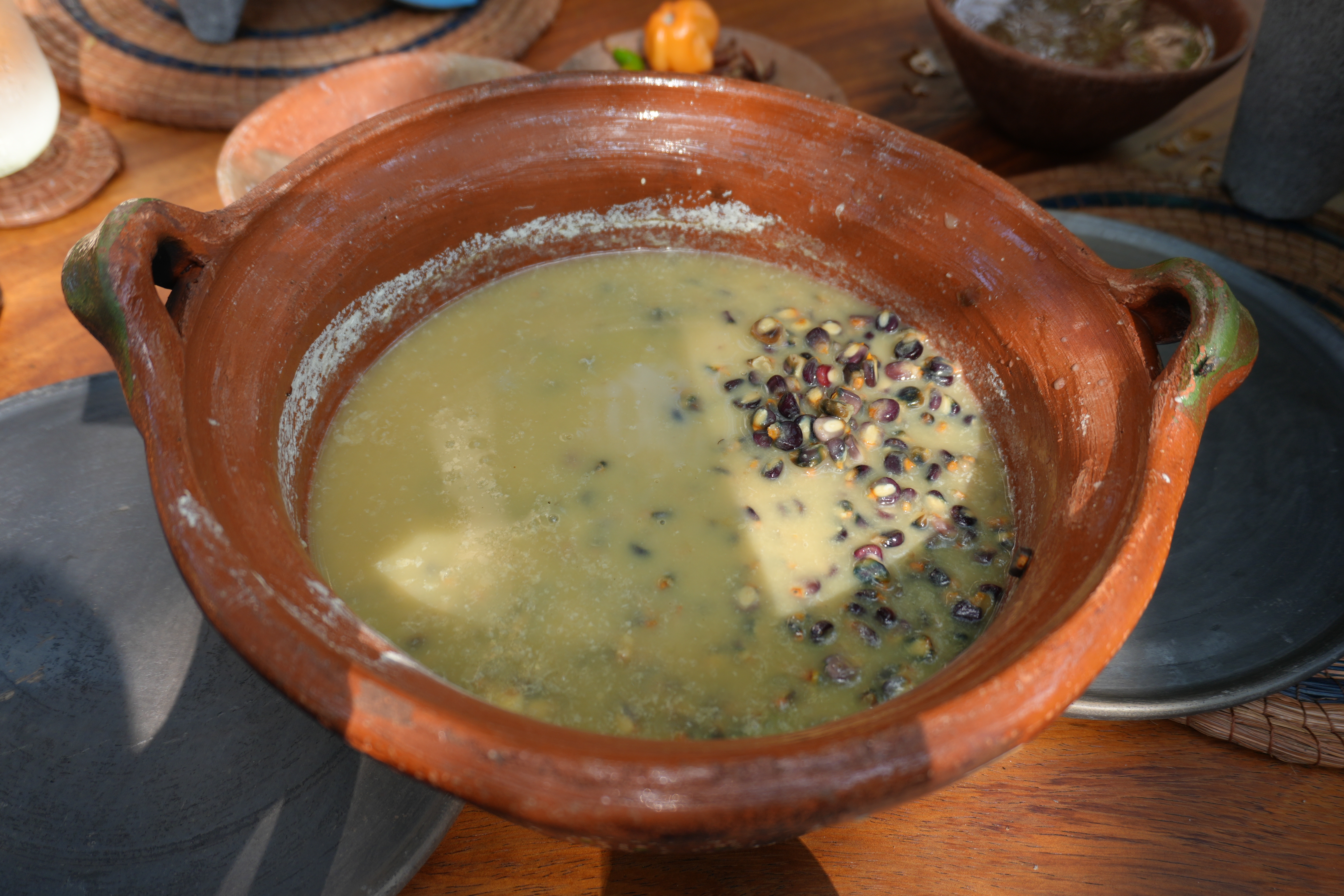 A clay bowl filled with a creamy soup featuring corn and beans, placed on a wooden table
