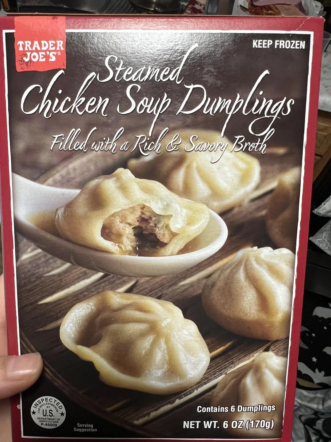 Package of Trader Joe&#x27;s steamed chicken soup dumplings, featuring an image of dumplings on a spoon and the package font highlighting the filling described