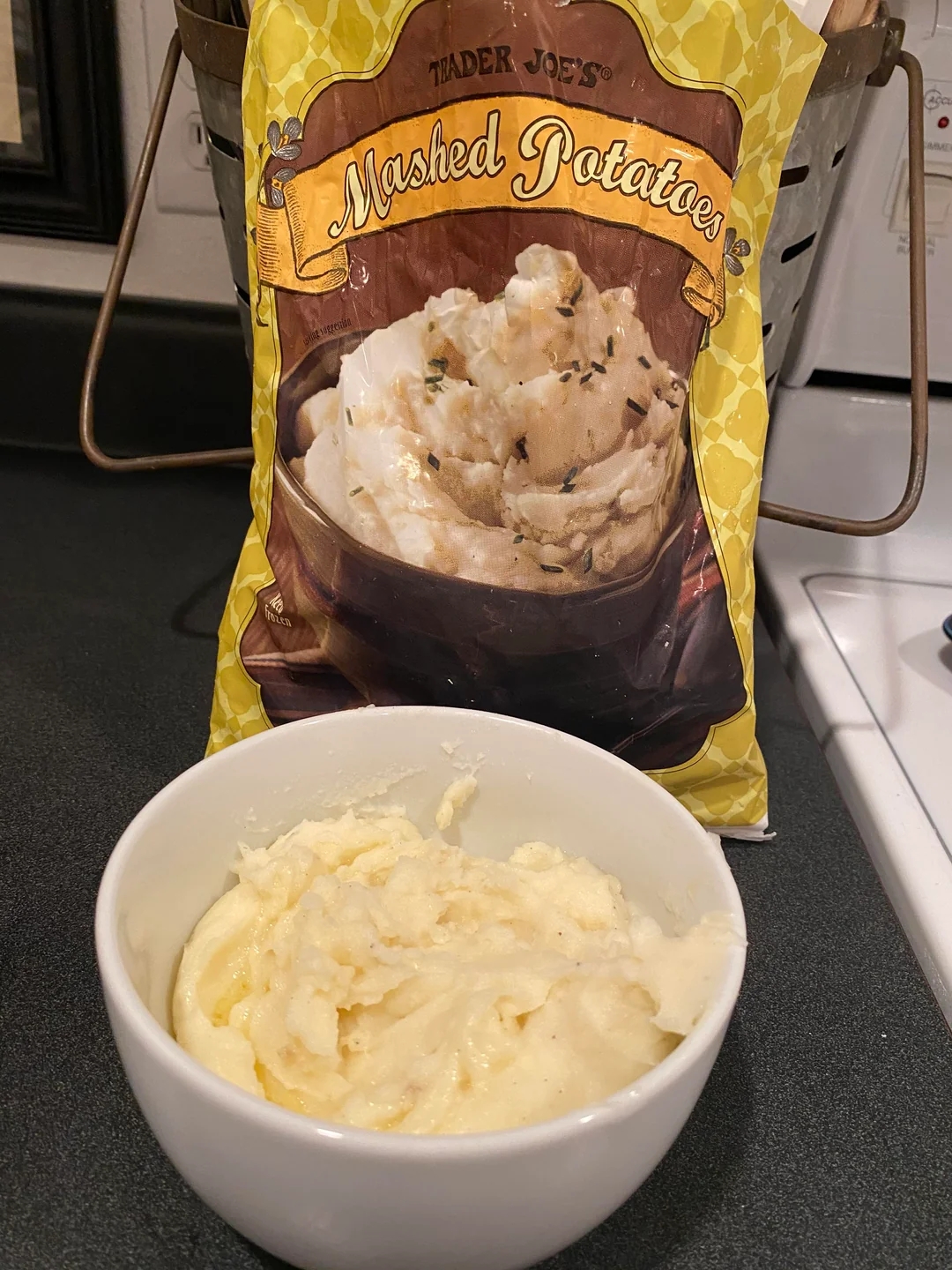 Bowl of creamy mashed potatoes in front of a Trader Joe&#x27;s mashed potatoes package on a kitchen counter
