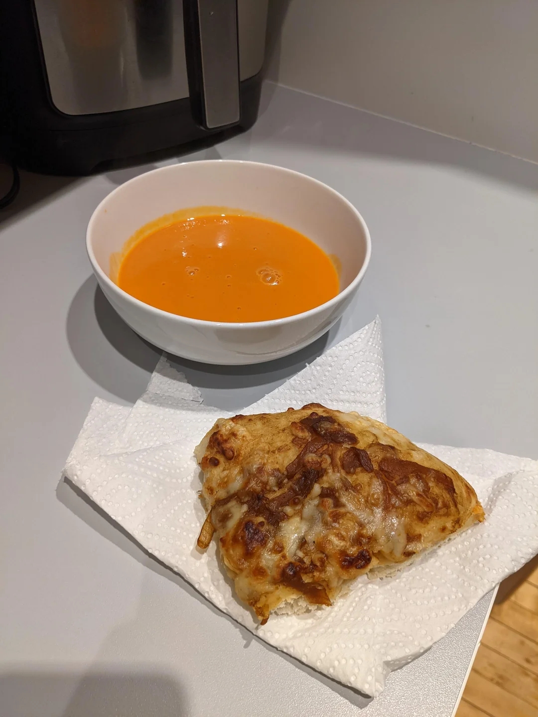 A bowl of soup next to a piece of cheesy bread on a napkin, set on a kitchen counter