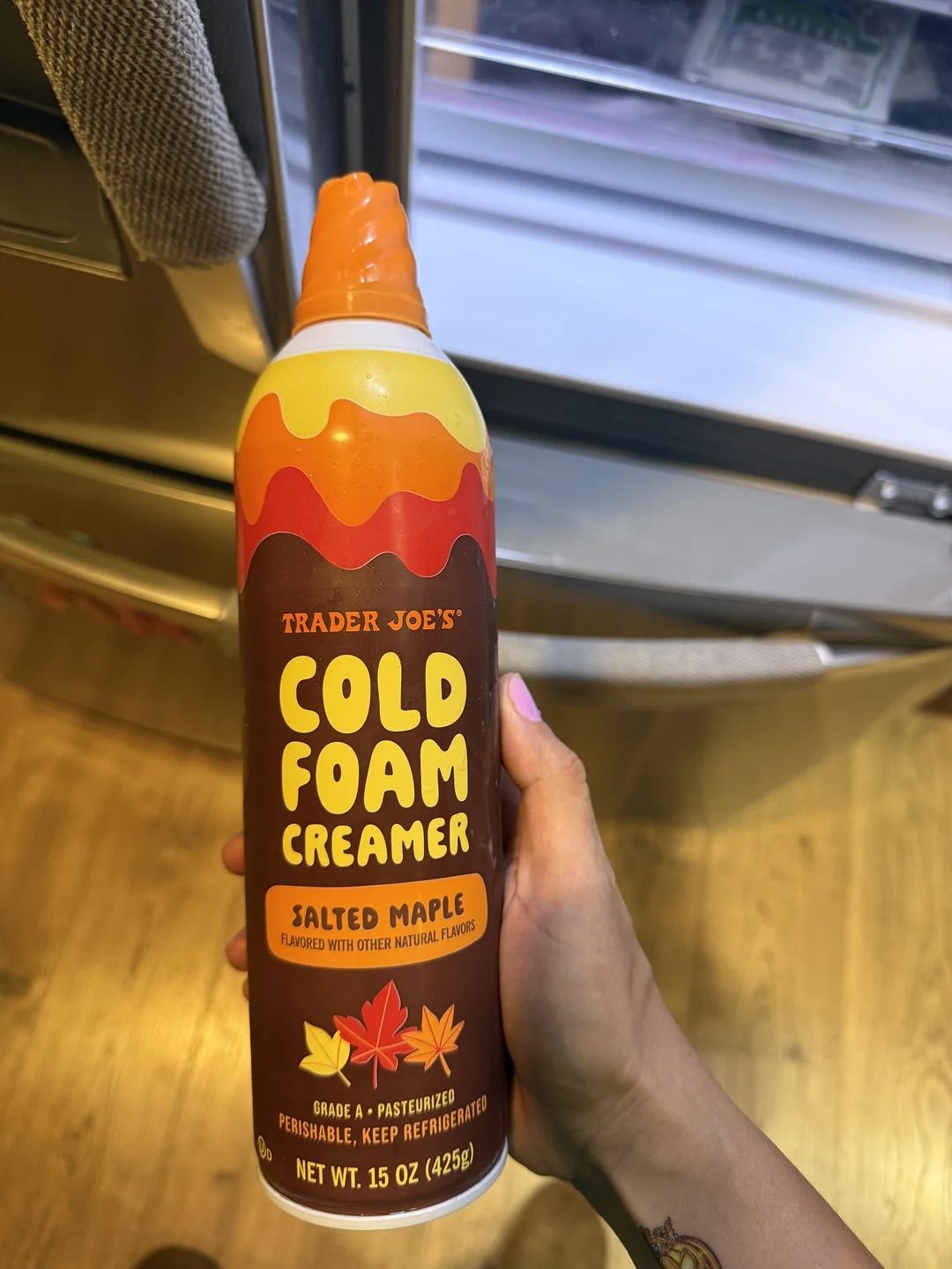A person holds a bottle of Trader Joe&#x27;s Cold Foam Creamer, Salted Maple flavor, in a kitchen setting