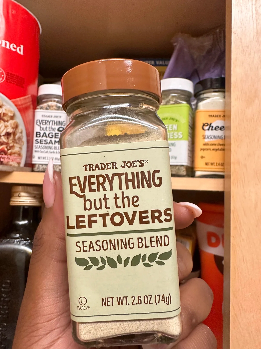 A hand holds a jar of Trader Joe’s “Everything but the Leftovers” seasoning blend in a pantry