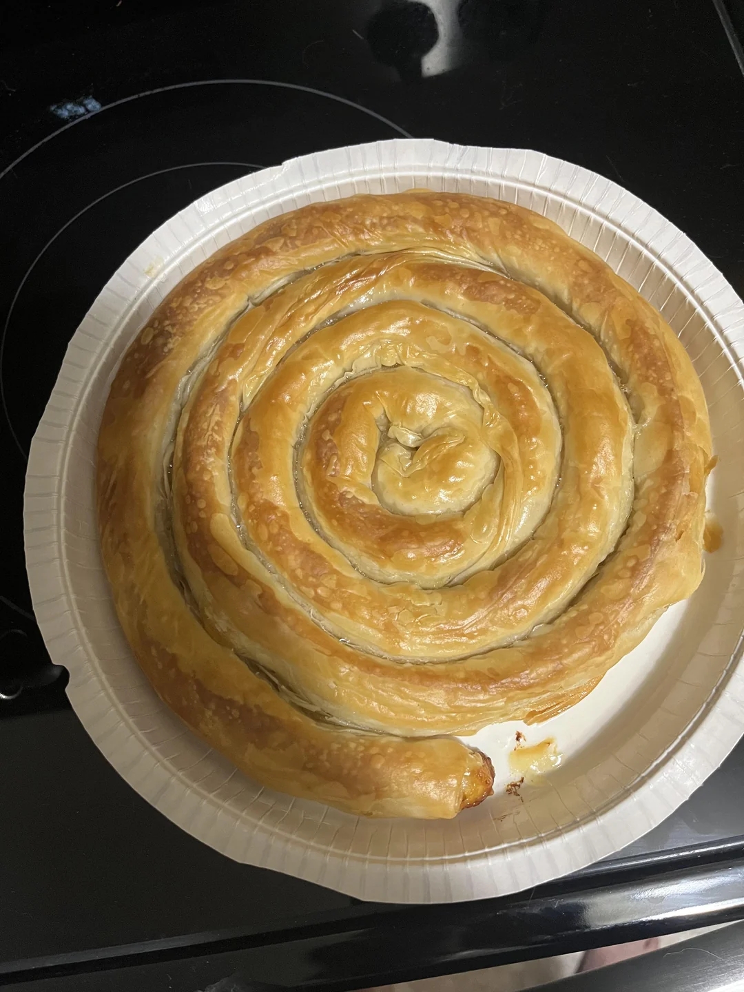 A plated spiral-shaped pastry with golden, flaky layers, resembling a large cinnamon roll