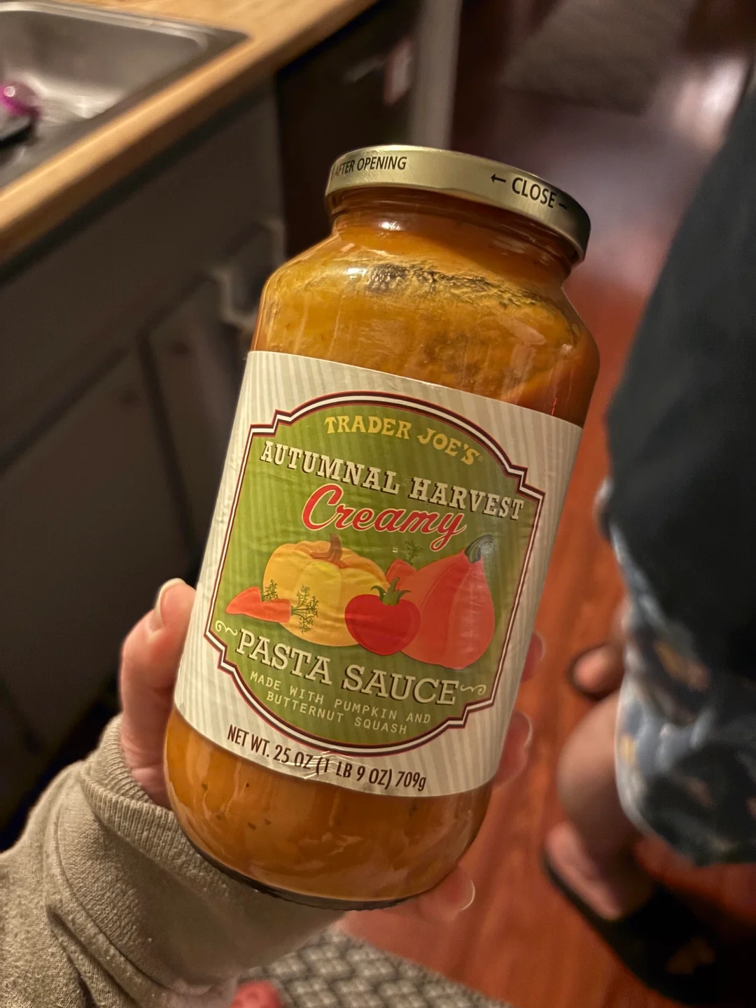 Person holding a jar of Trader Joe&#x27;s Autumnal Harvest Creamy Pasta Sauce in a kitchen