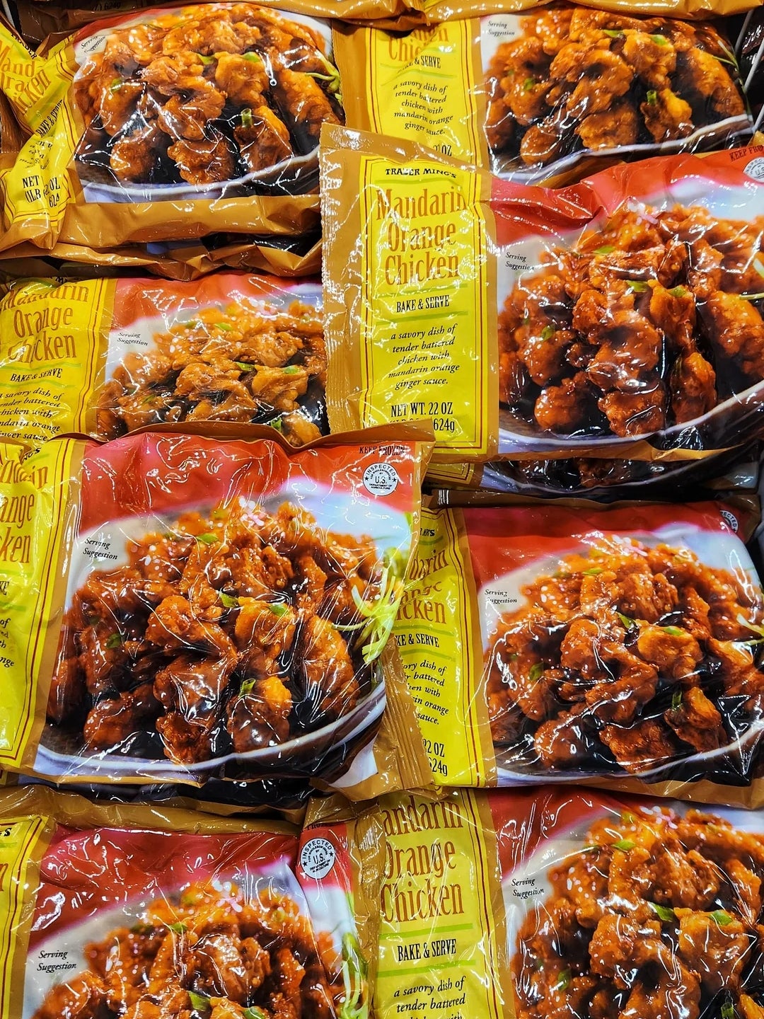 Bags of frozen mandarin orange chicken in a grocery store freezer, stacked and displayed for sale