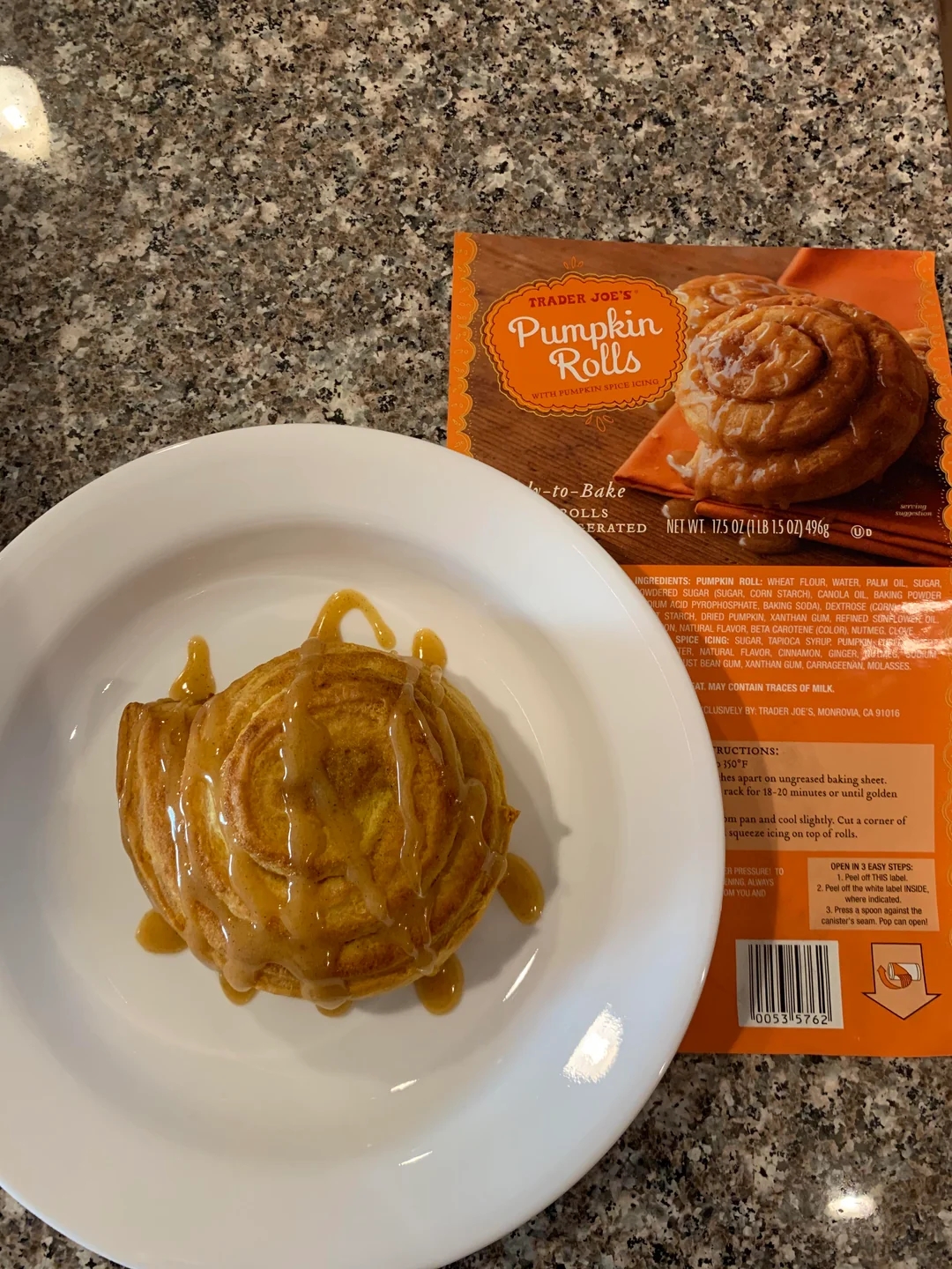 Pumpkin roll with caramel drizzle on a white plate next to Trader Joe&#x27;s pumpkin rolls package on a marble countertop