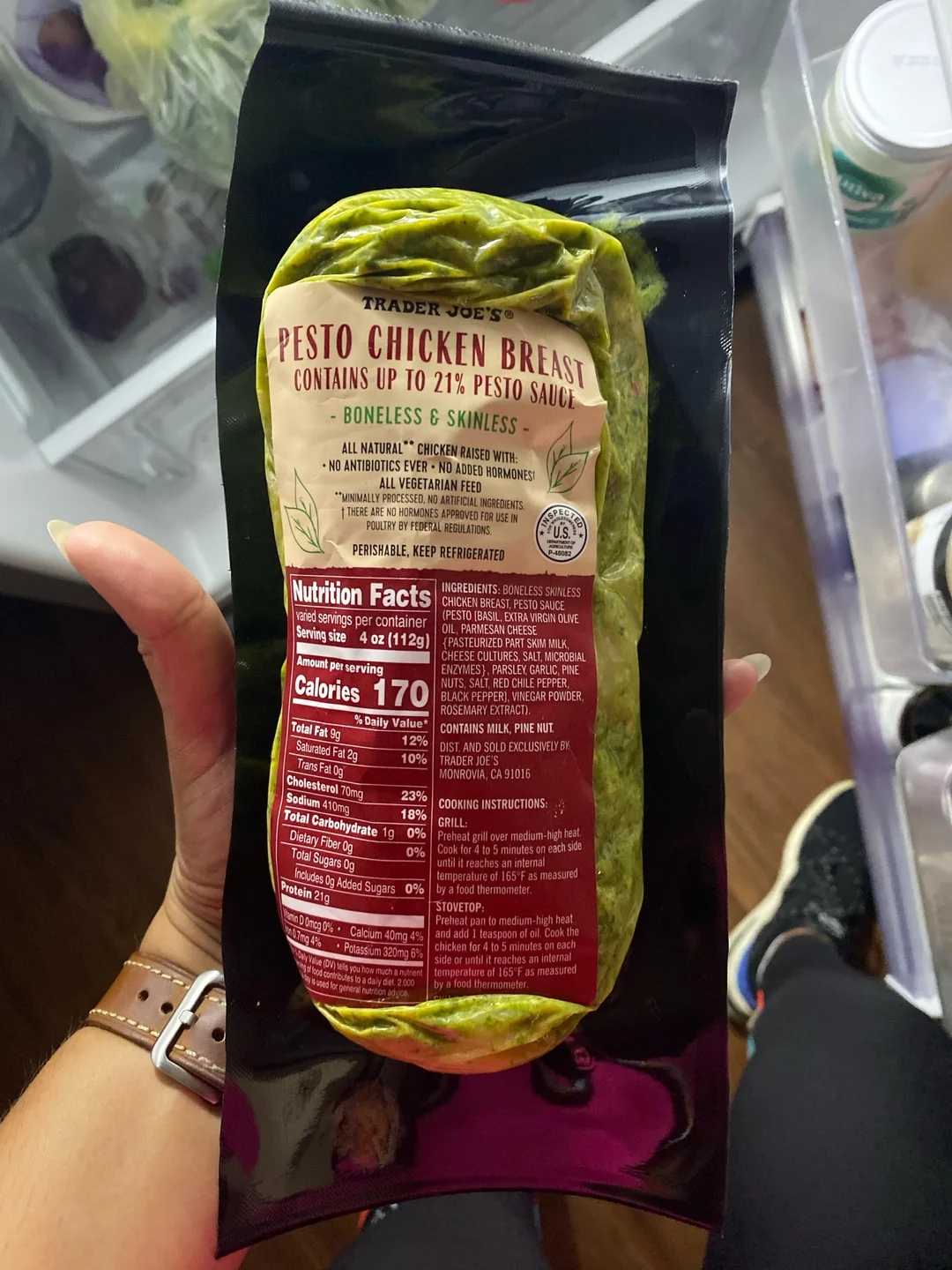 Package of Trader Joe&#x27;s pesto chicken breast held over an open fridge, showing nutrition facts and highlighting its pesto sauce content