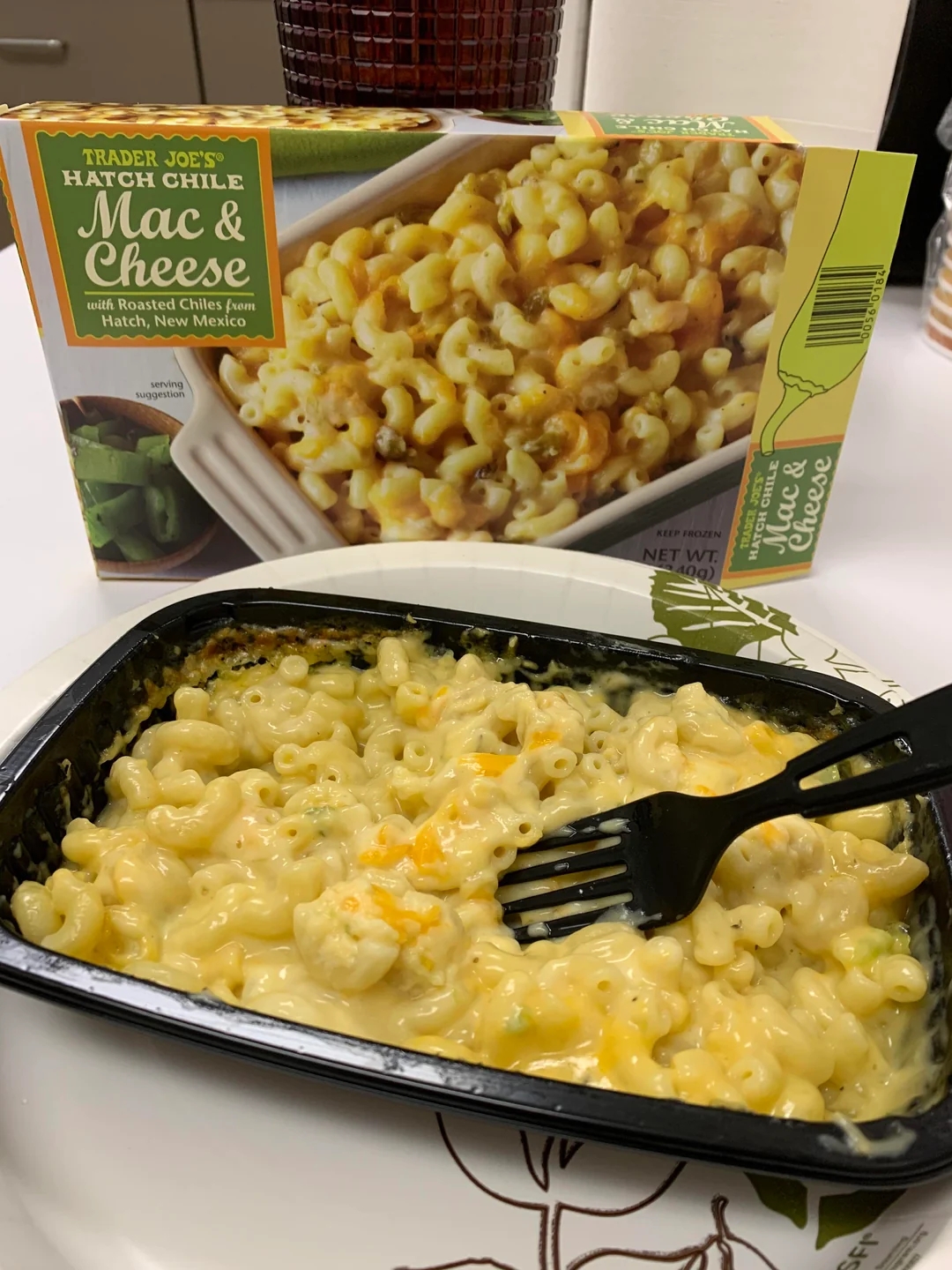 Tray of Trader Joe&#x27;s Hatch Chile Mac &amp;amp; Cheese with fork is shown in front of its packaging, highlighting the meal&#x27;s cheesy appearance