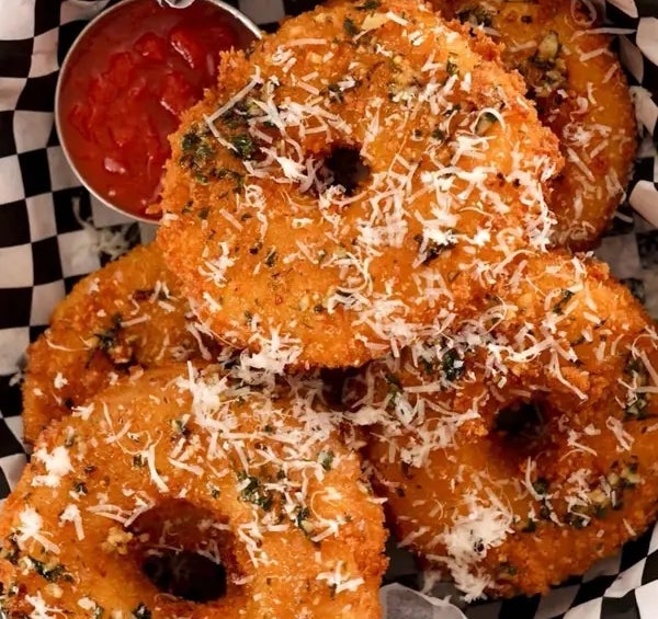 Crispy fried onion rings topped with grated cheese, garnished with herbs, served in a basket with a side of ketchup