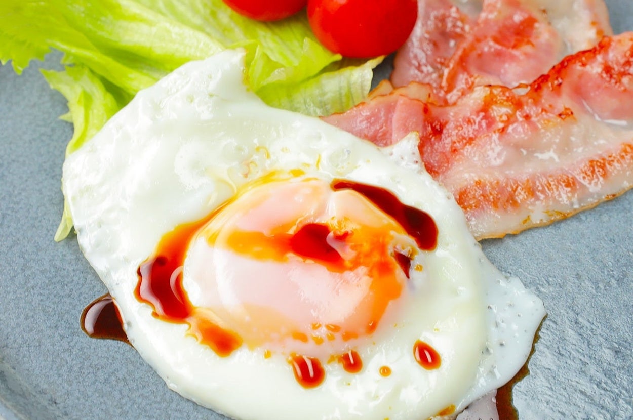 朝食のプレートにベーコン、目玉焼き、レタス、トマトがのっている。
