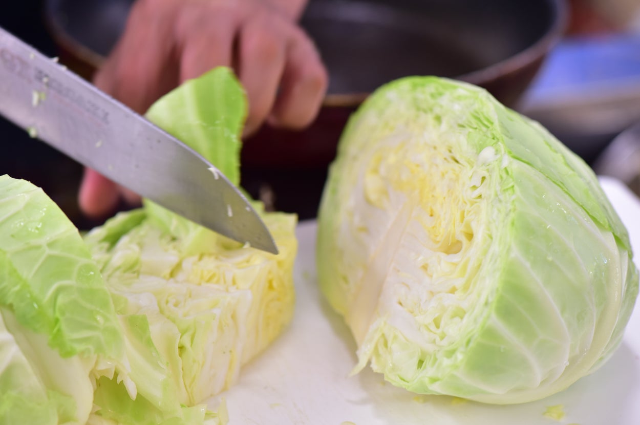 キャベツを切っている手元。ナイフがキャベツに入っている。