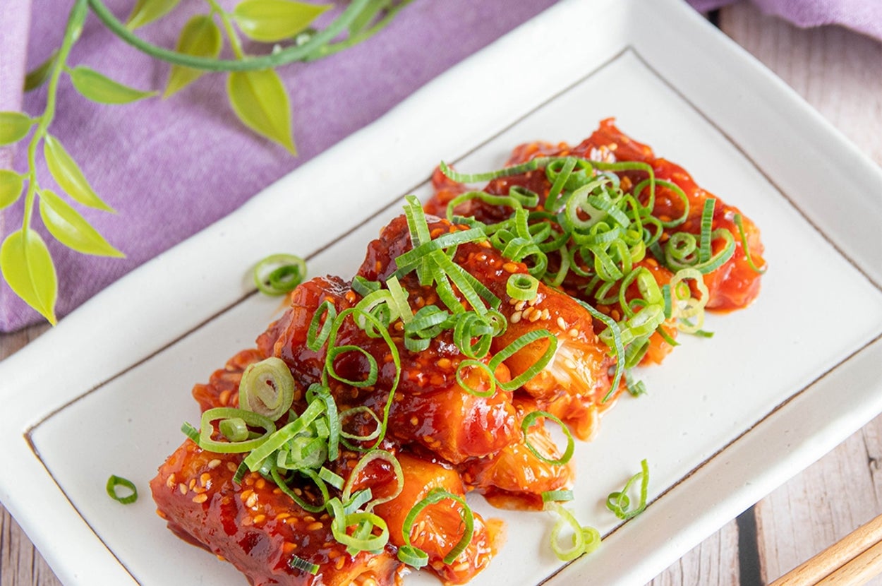 白い皿に盛られたちくわ料理、ねぎがトッピングされている。紫の布と緑の装飾が背景にある。