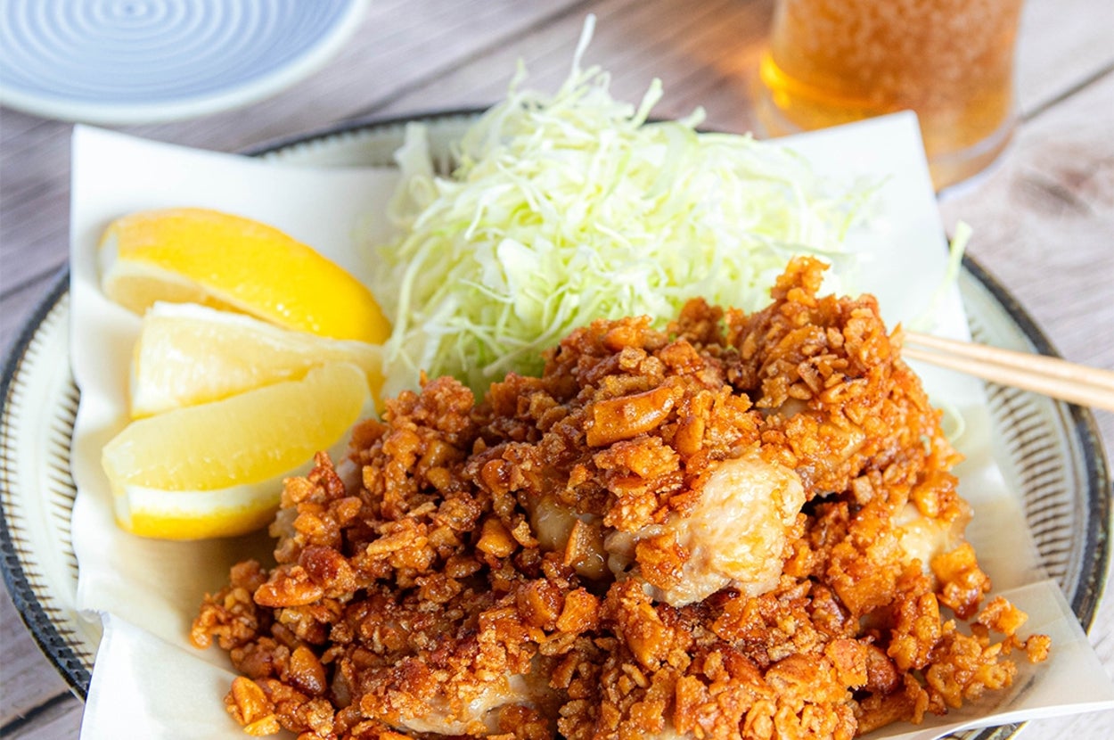 揚げた鶏肉の上にかりっとした衣がかかり、レモンとキャベツの千切りが添えられた料理。背景にビールのグラス。