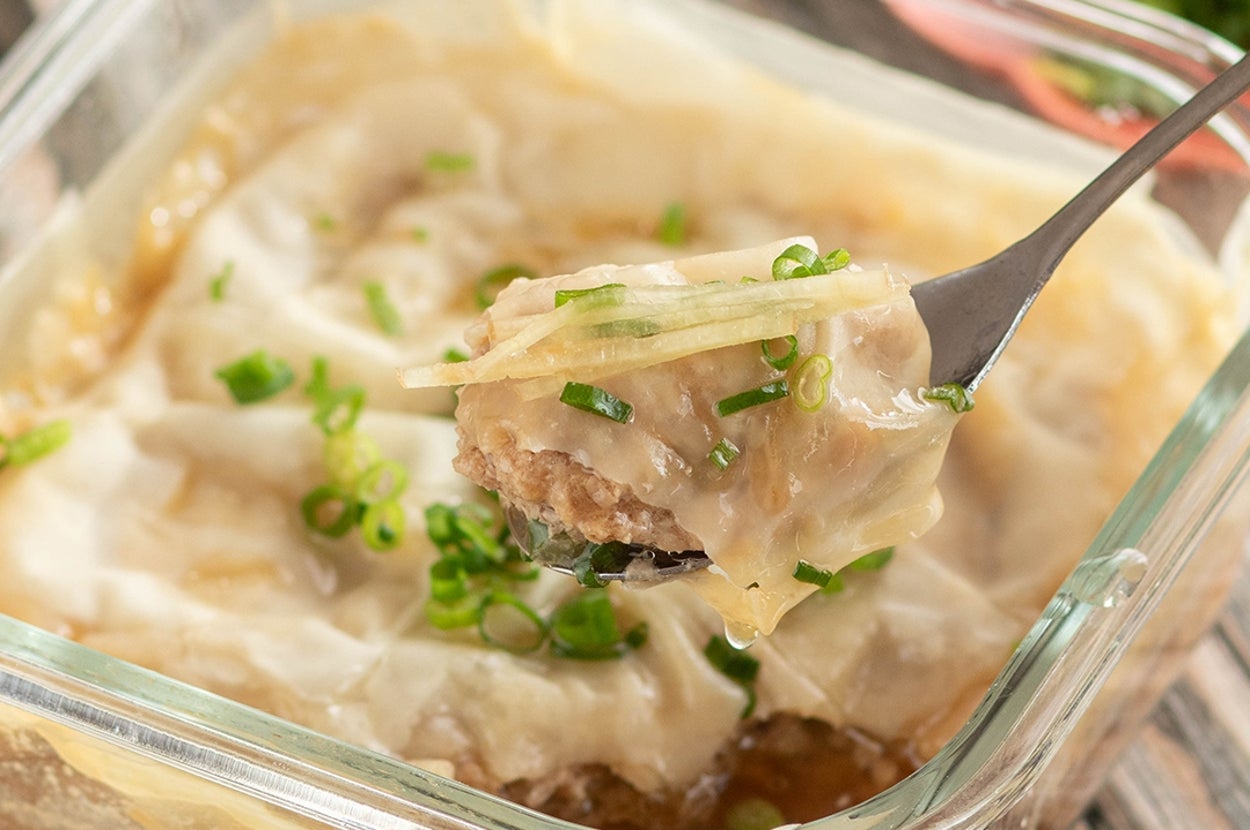 ガラス容器に入った中華風の蒸し料理。スプーンで持ち上げられた一口分には、ネギとショウガがトッピングされています。