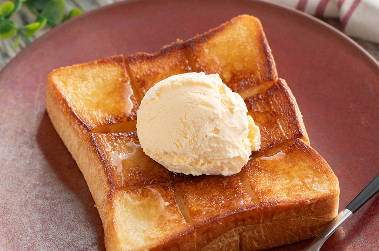 厚切りトーストにアイスクリームが乗っている。トーストは格子状に切り込みが入り、バターがしみ込んでいる。フォークが添えられている。