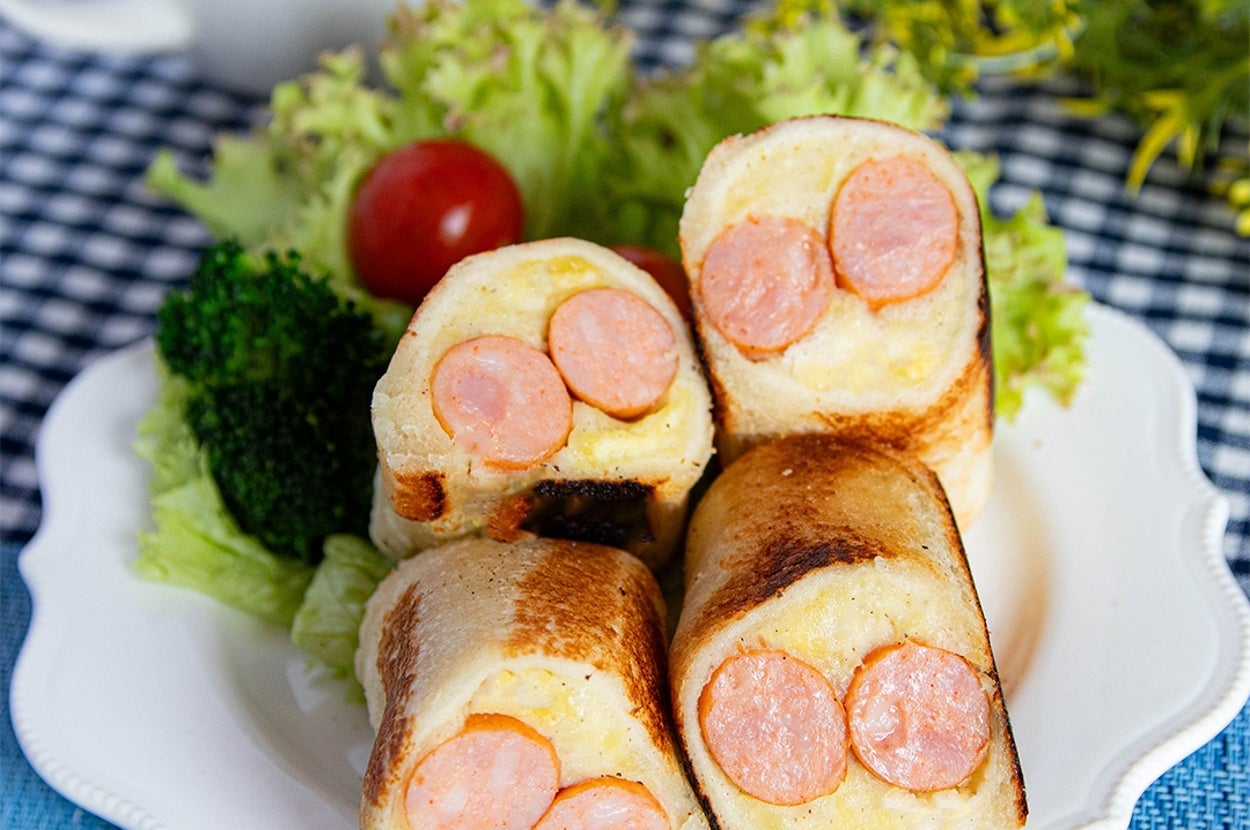 お皿に盛られたソーセージ入りパンロール。付け合わせにレタスとブロッコリーがあり、背景にカップが見える。