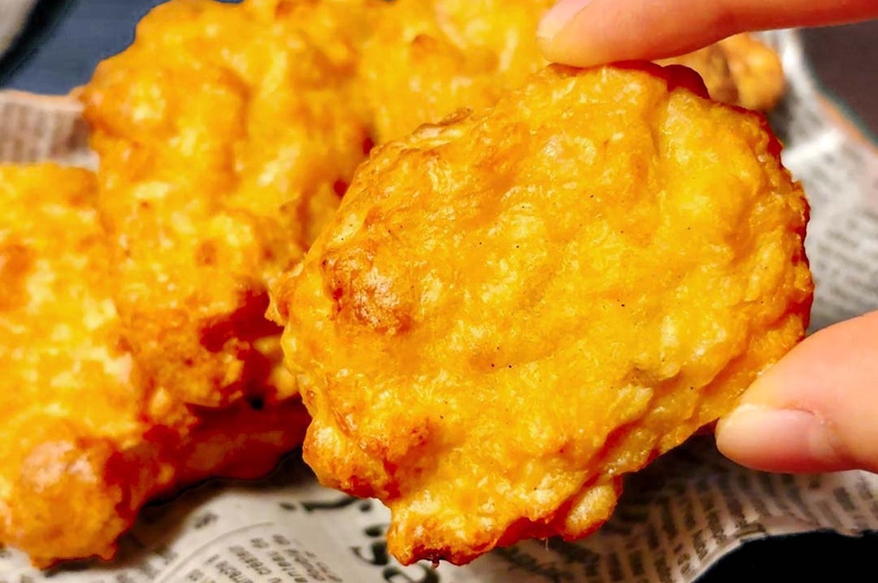 人が新聞の上に置かれた揚げられたナゲットをつまんでいる。食欲をそそる光景。