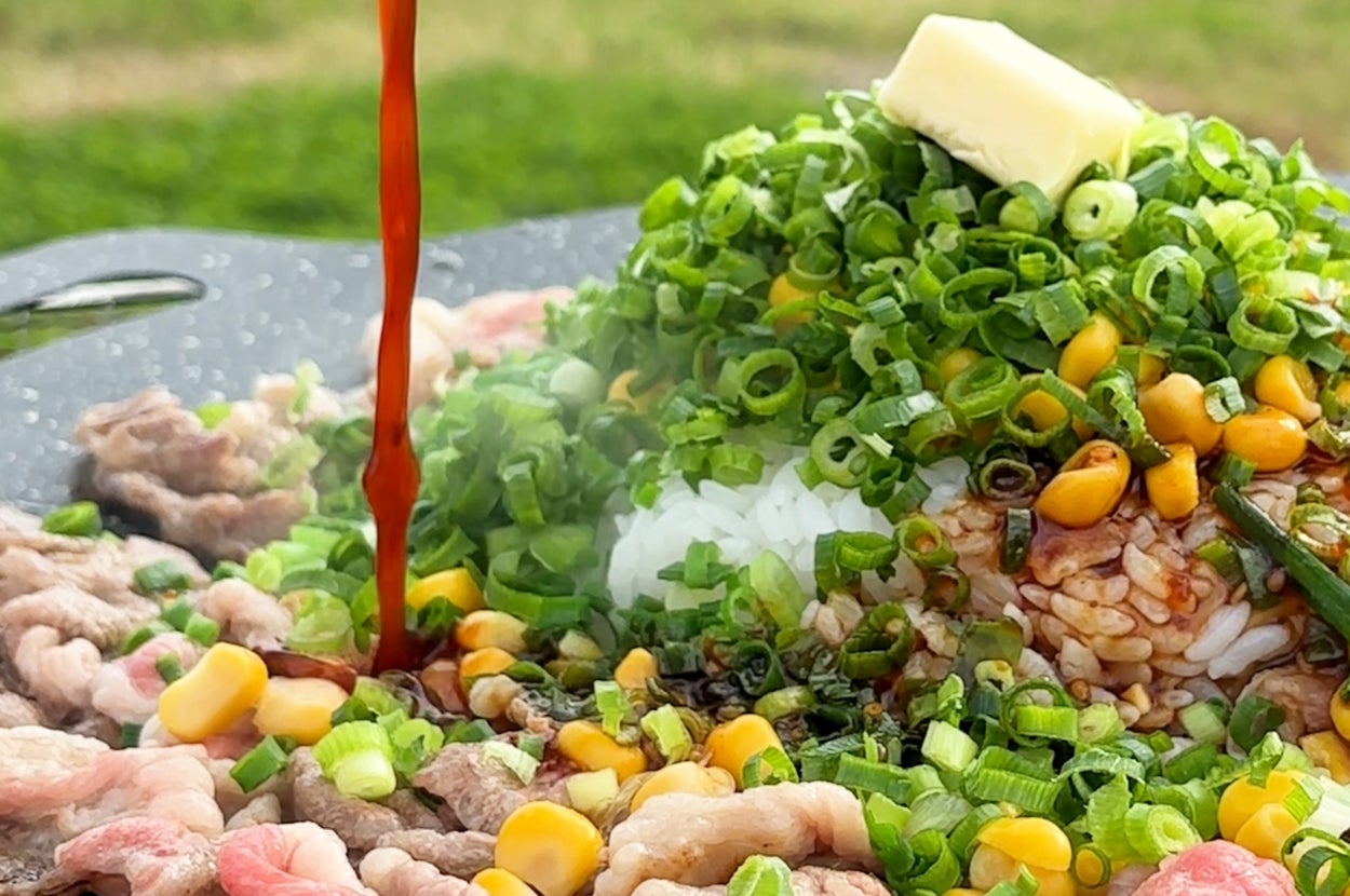 薄切り肉とネギの上にご飯が盛られ、ソースがかけられているシズル感のある料理。