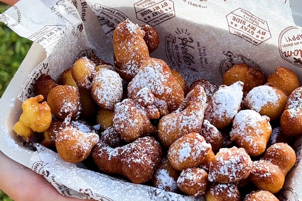 手に持たれた紙に包まれた粉砂糖がかかった揚げ菓子がたくさん見えます。
