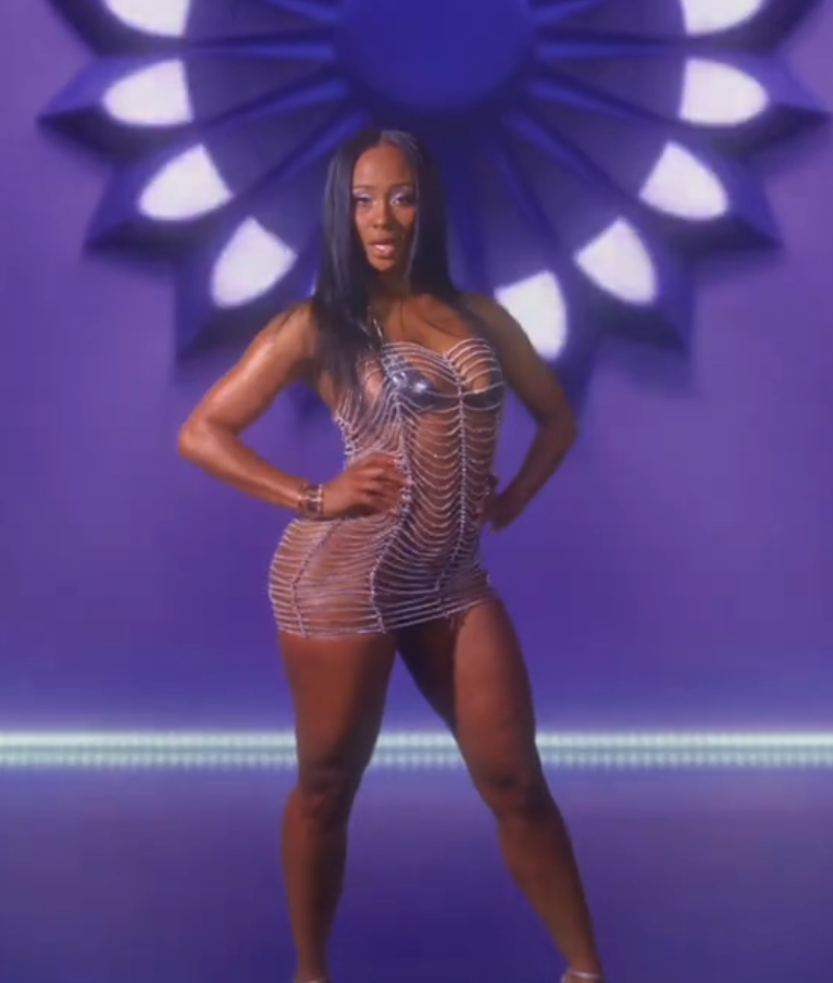 Person in a form-fitting, web-patterned dress poses confidently against a decorative background