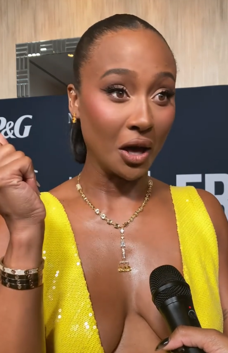Person in elegant dress on red carpet holding a microphone, expressing surprise or excitement