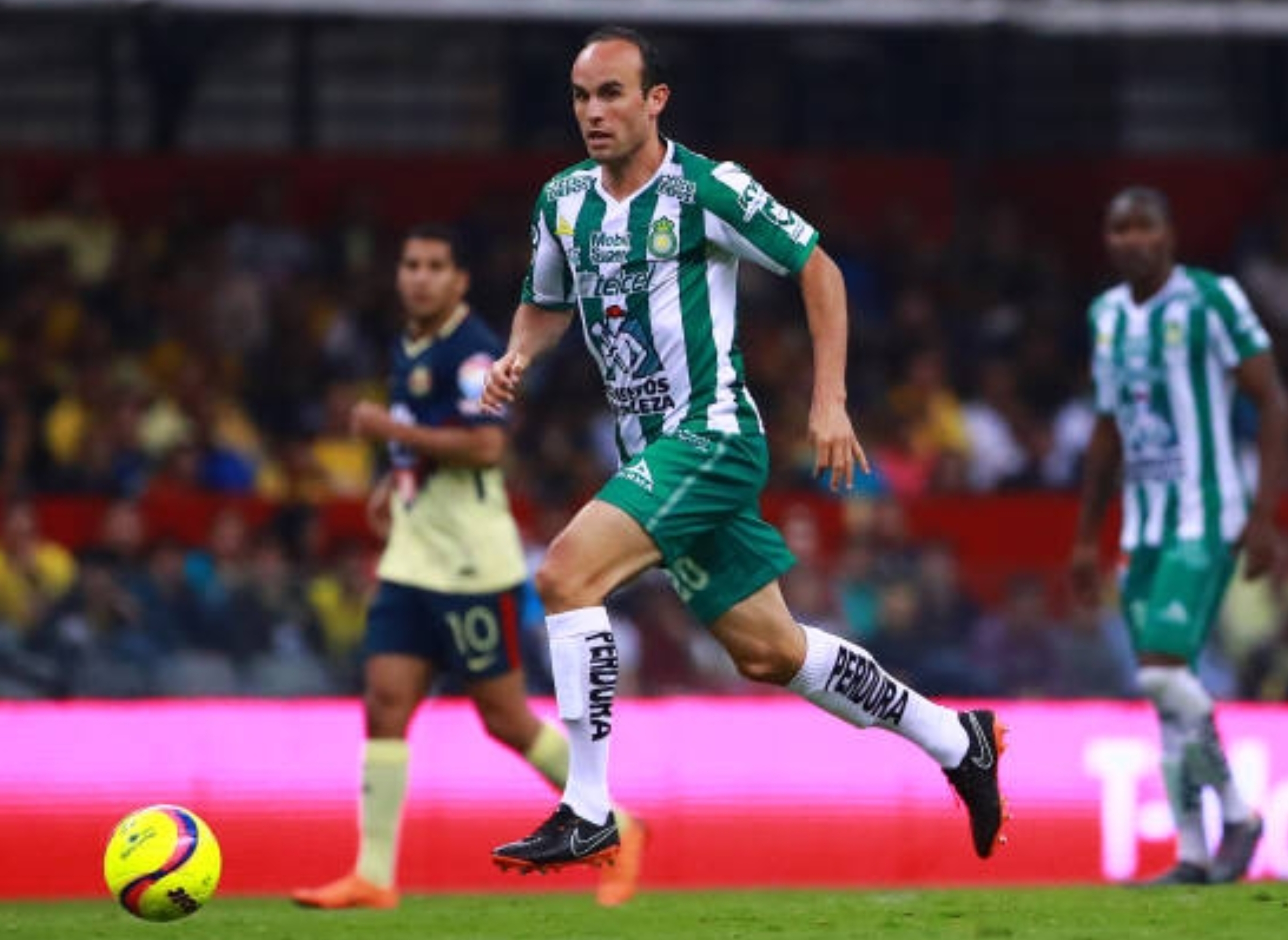 Soccer player in green and white kit dribbles the ball on field during a match, with stadium audience in background