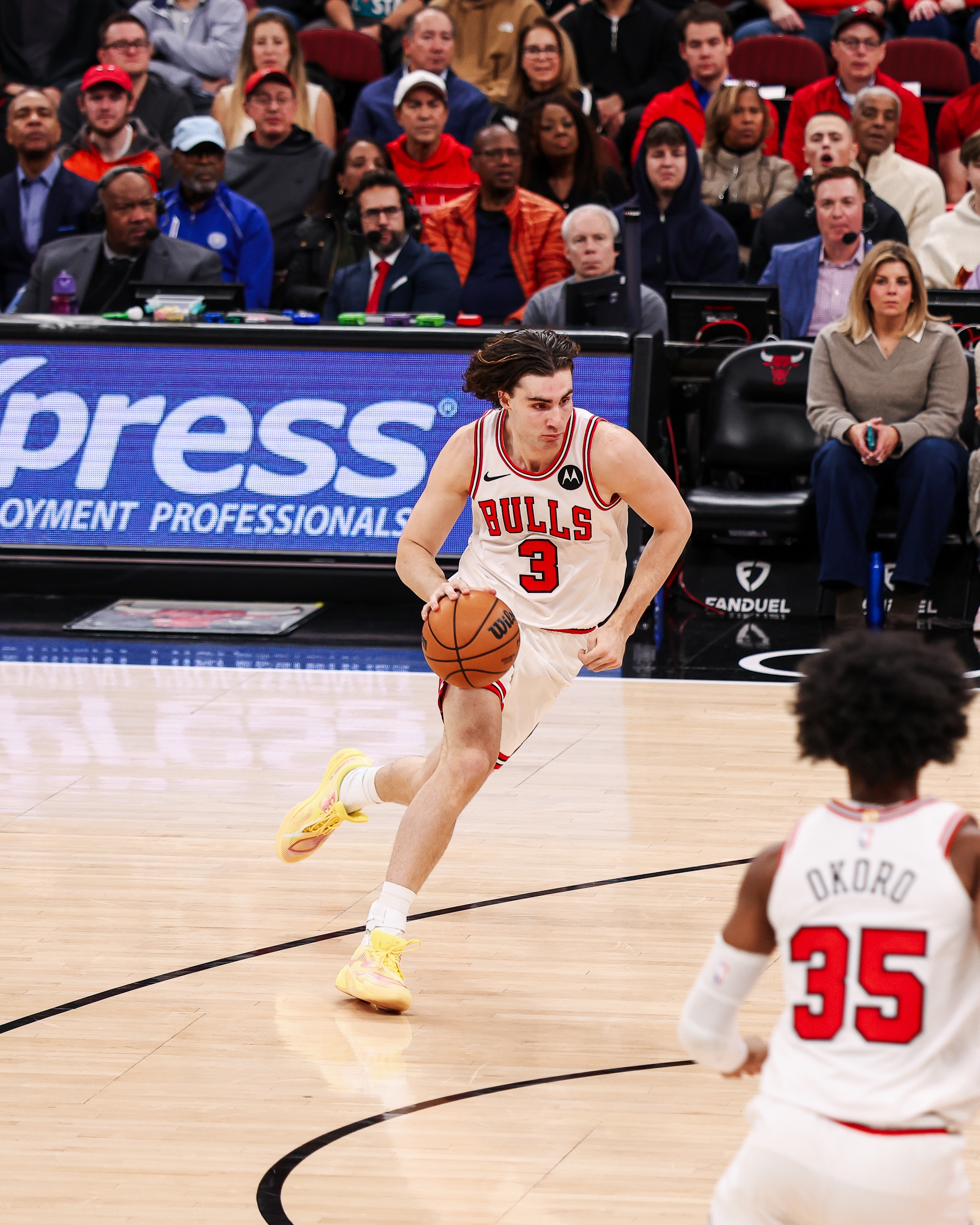 Basketball player in white Bulls uniform dribbles during a game with spectators watching from the stands