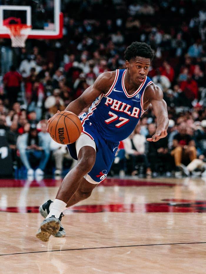 Basketball player in a &quot;PHILA 77&quot; jersey dribbling on a court during a game