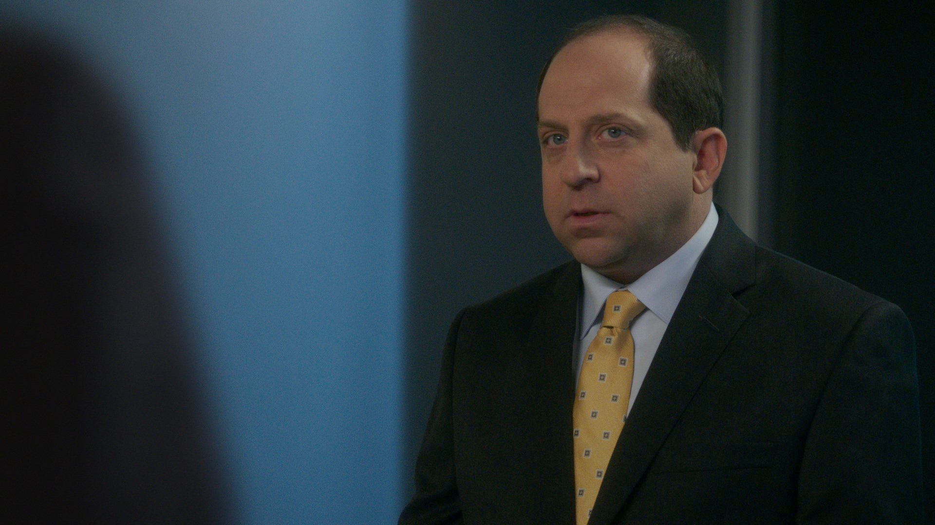 A idiosyncratic   successful  a suit   and necktie  stands indoors, looking intently to the side