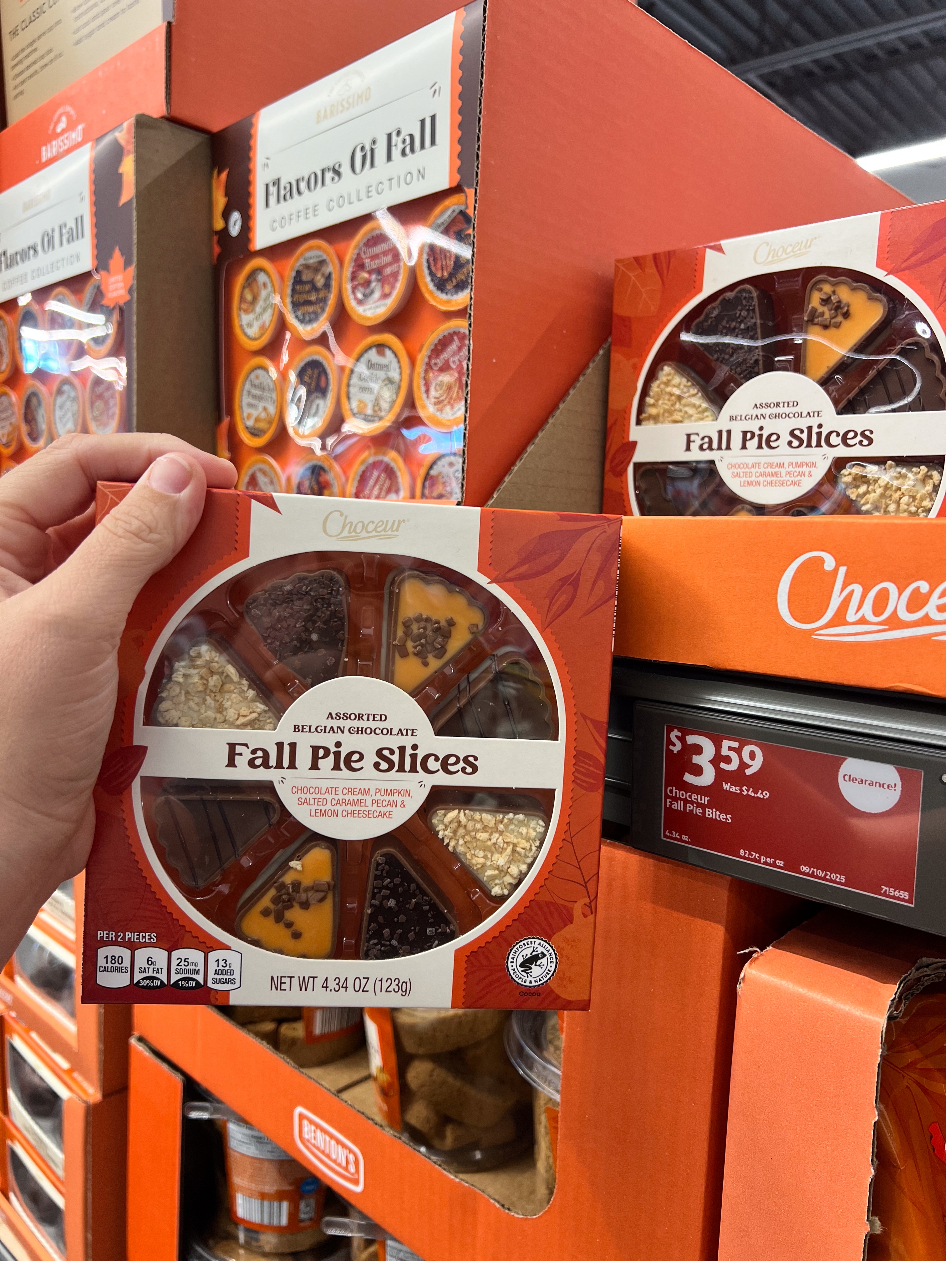 Person holding a package of assorted Fall Pie Slices, made of Belgian chocolate, in a grocery store display with similar items