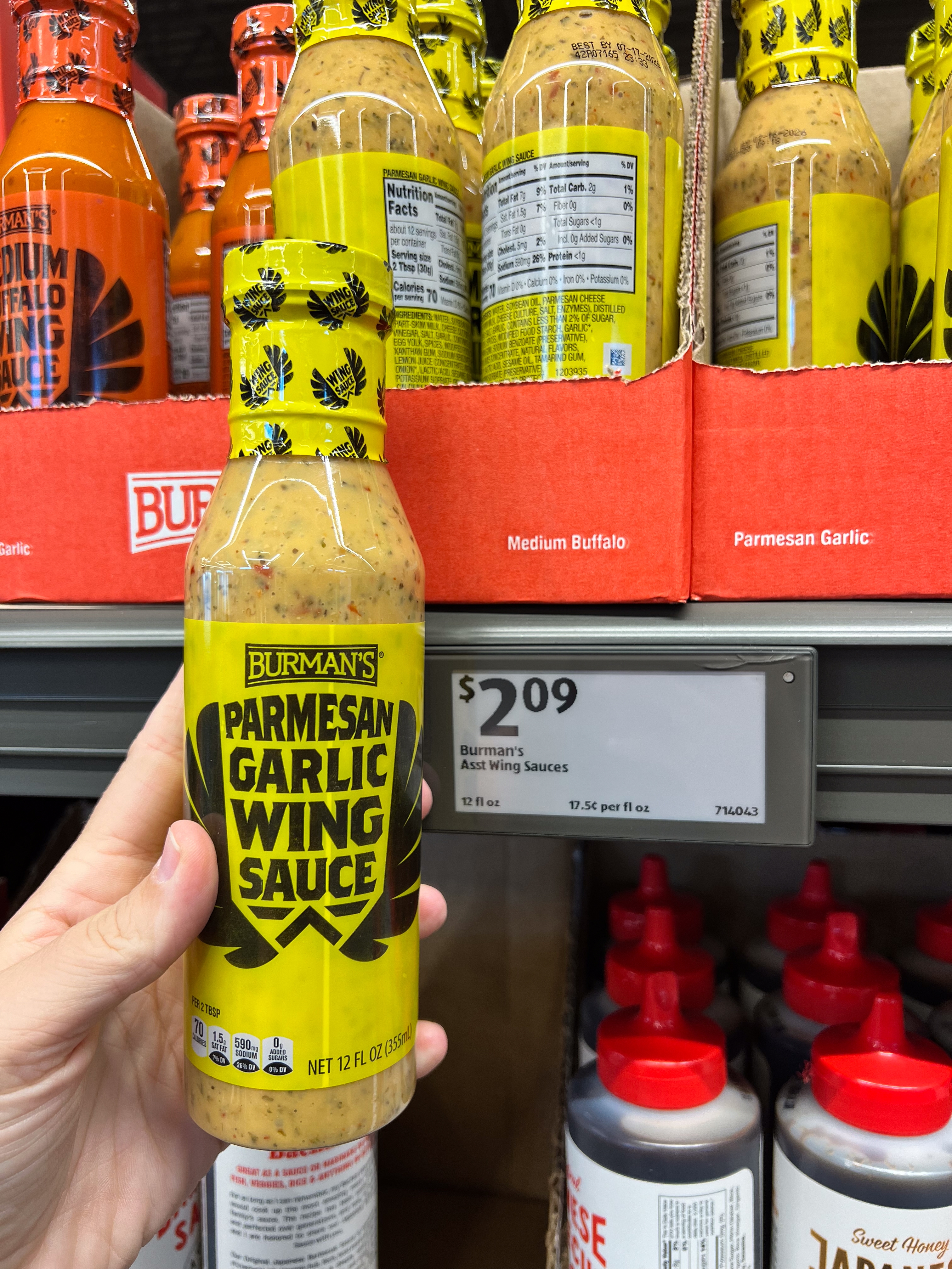 A person holds a bottle of Burman&#x27;s Parmesan Garlic Wing Sauce in a store. Price tag reads $2.09 for a 12 fl oz bottle