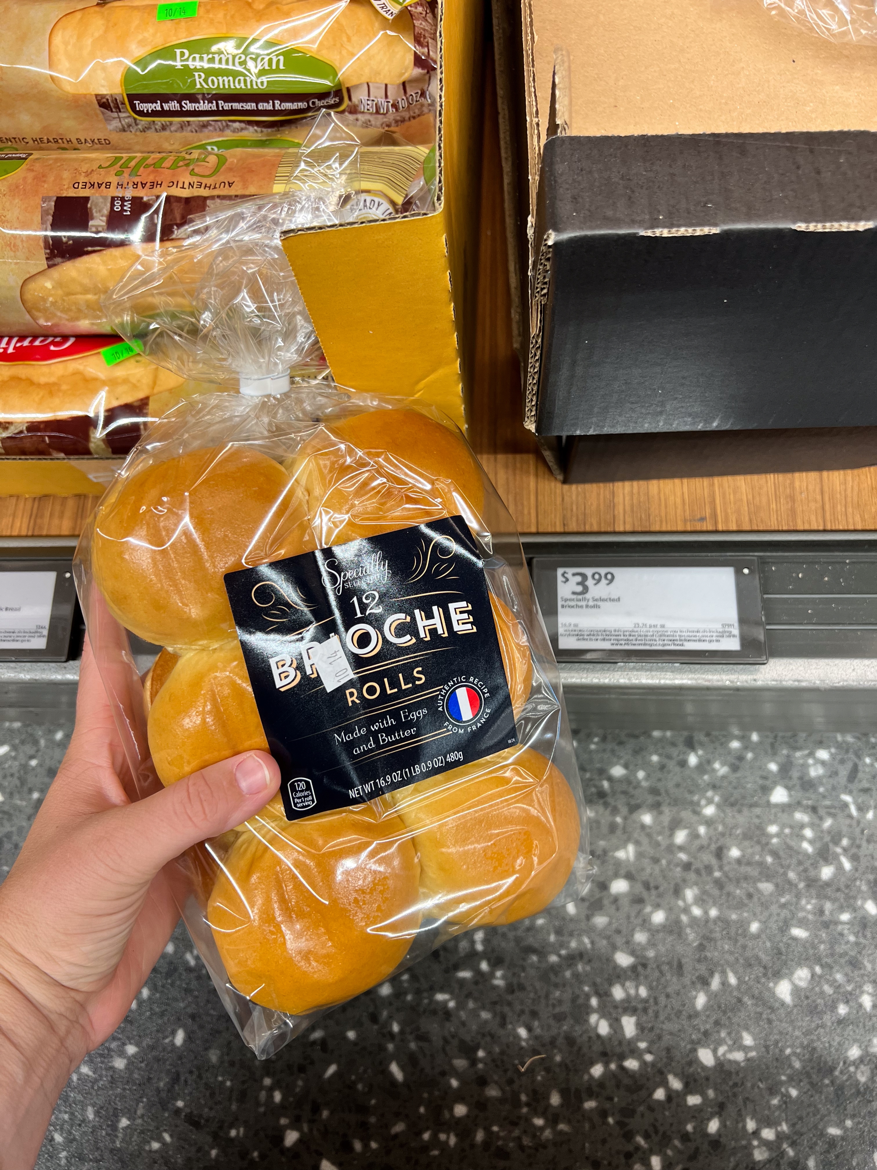 Person holds a pack of 12 brioche rolls in a grocery store, next to a price label showing $3.99