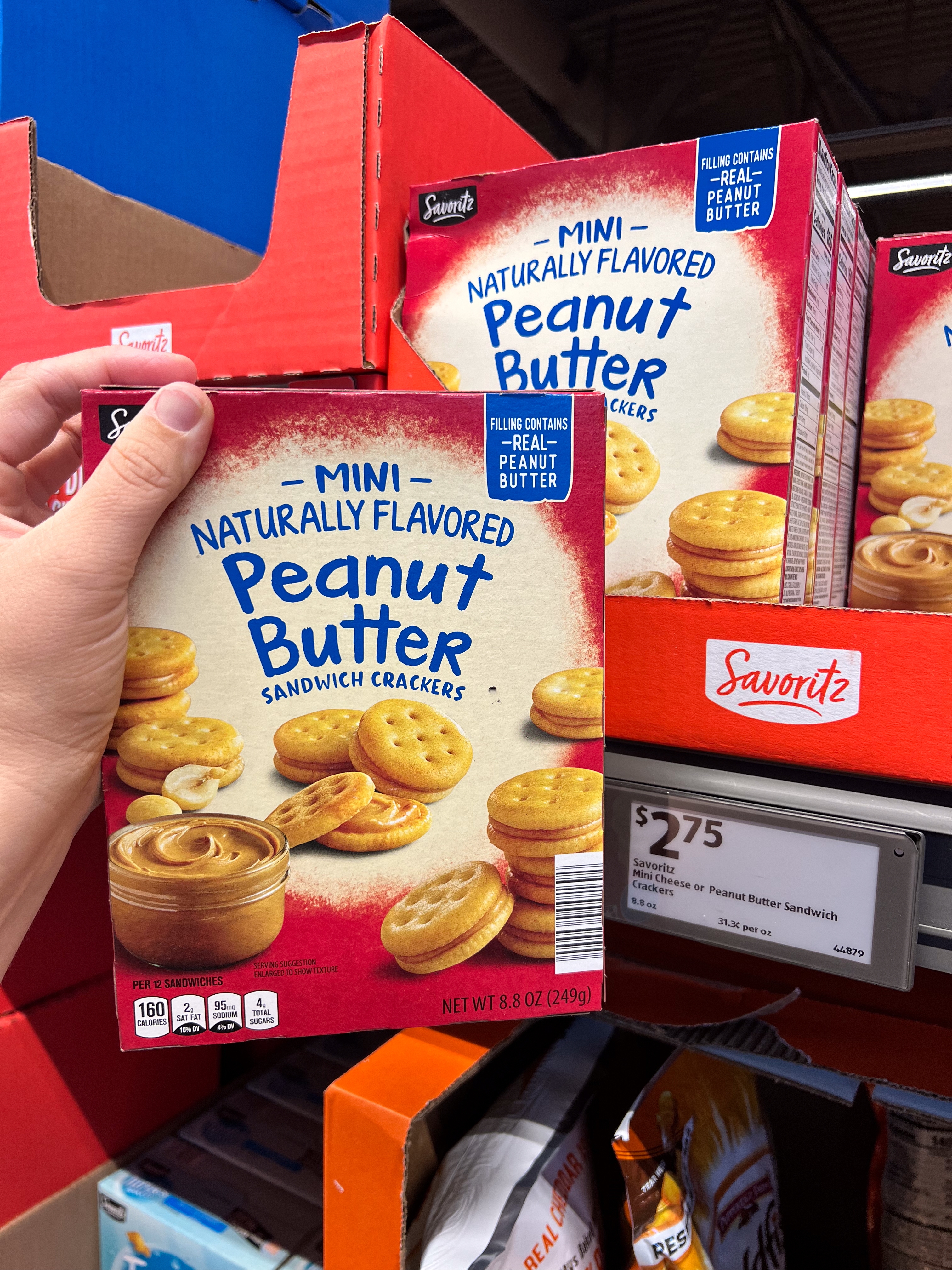Hand holds a box of Savoritz Mini Peanut Butter Sandwich Crackers in a store, priced at $2.75