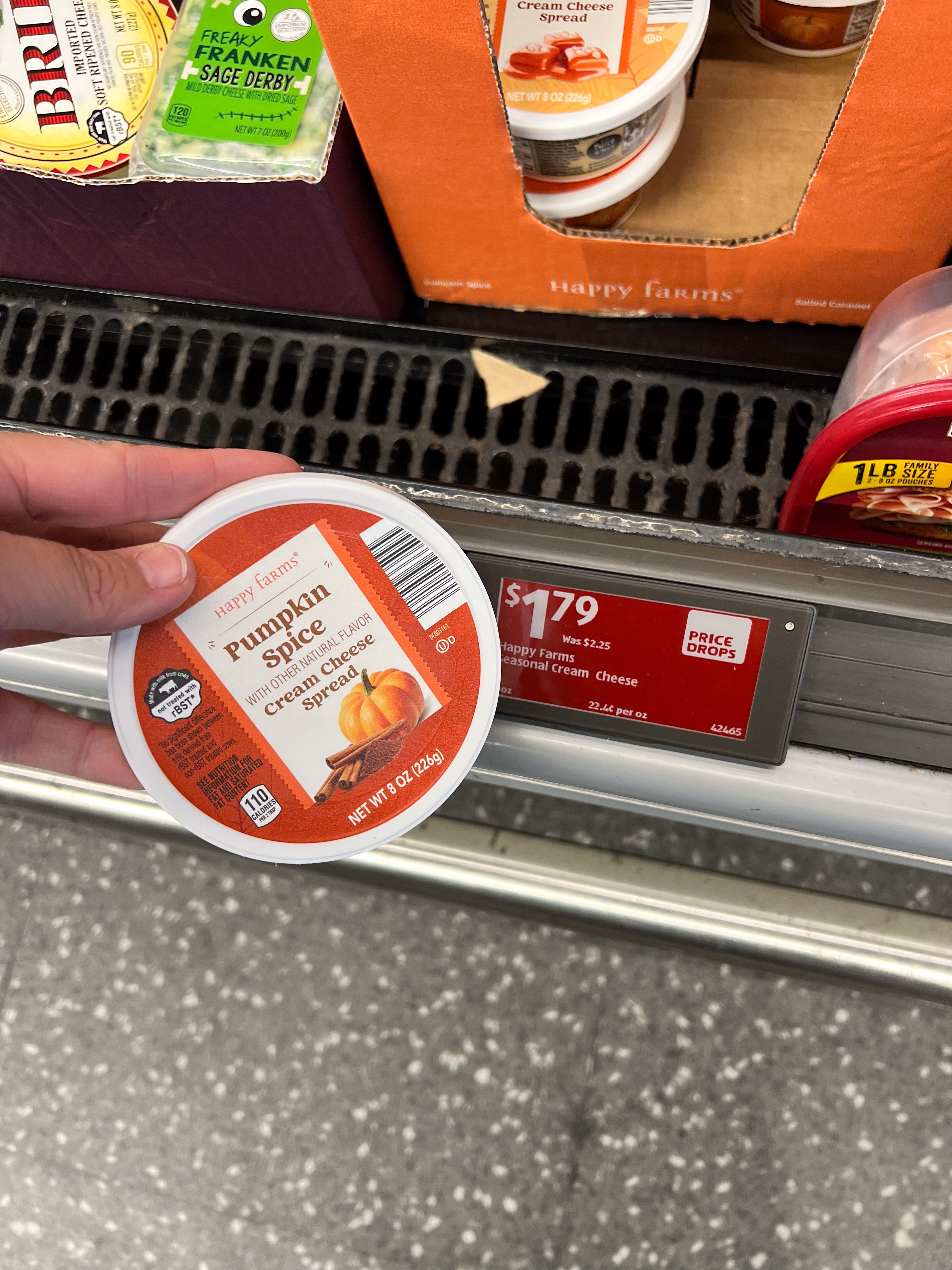 Person holding a container of pumpkin spice cream cheese priced at $1.79 on a store shelf