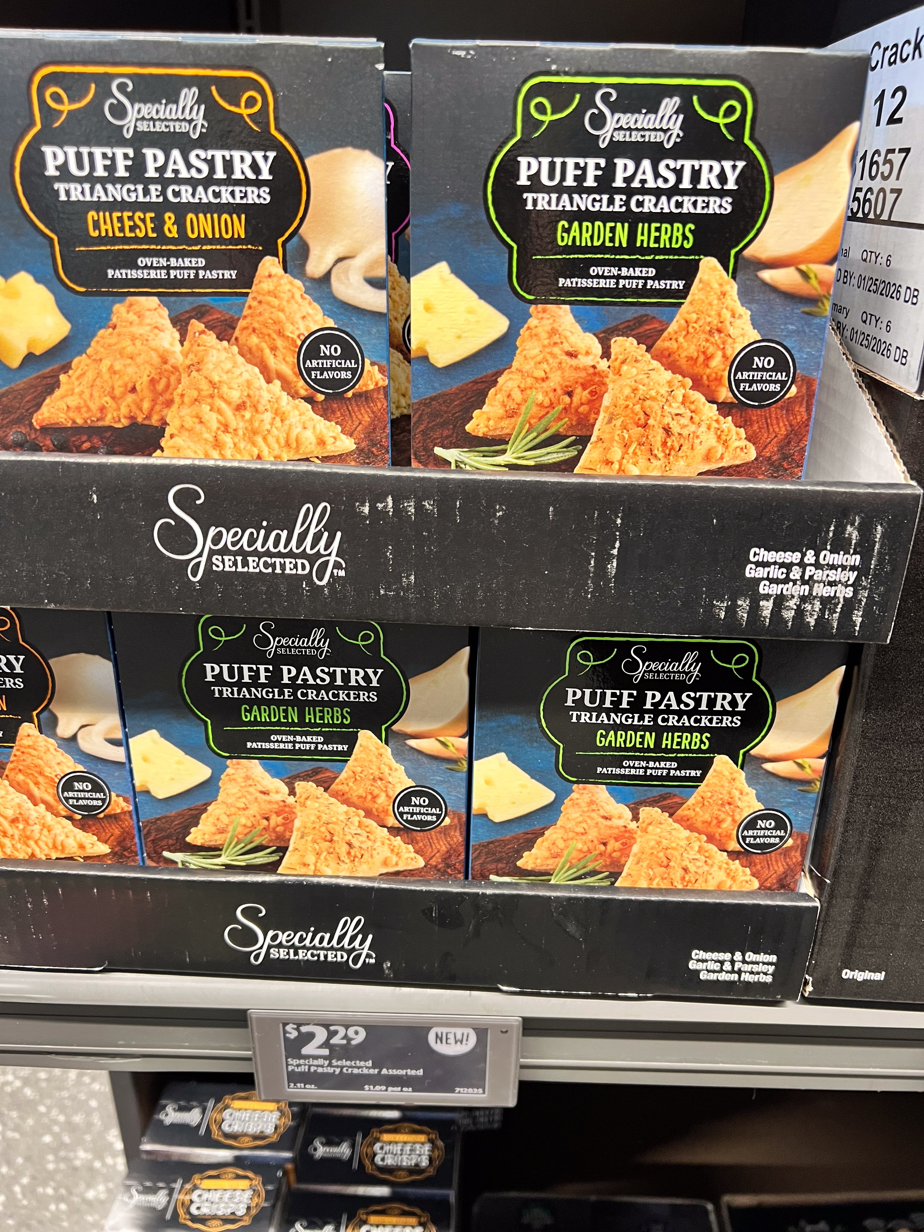 Boxes of puff pastry triangle crackers in cheese &amp;amp; onion and garden herbs flavors stacked on a store shelf. Price shown: $2.29