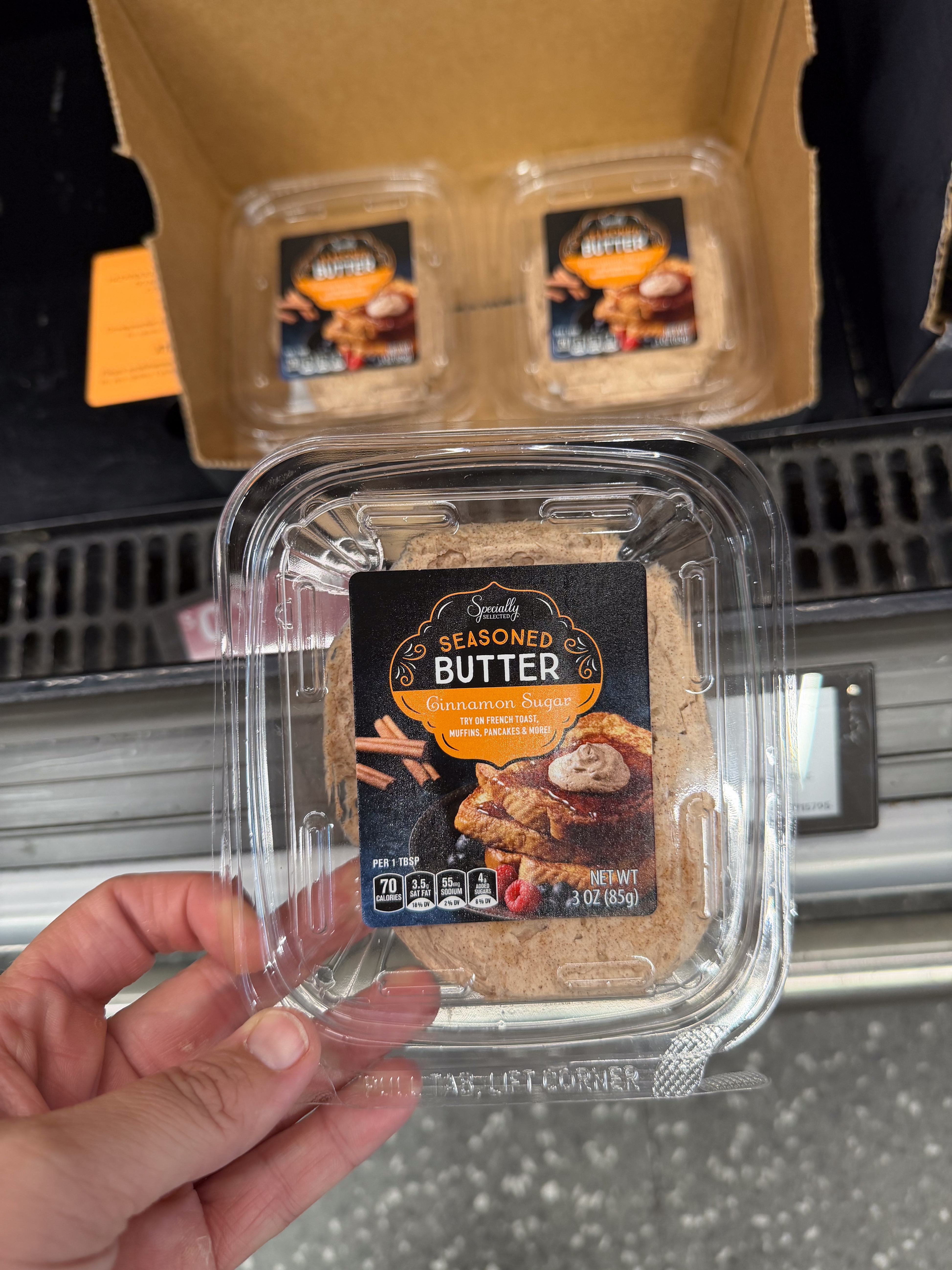 Hand holding a plastic container of cinnamon sugar seasoned butter, with more containers visible in the background