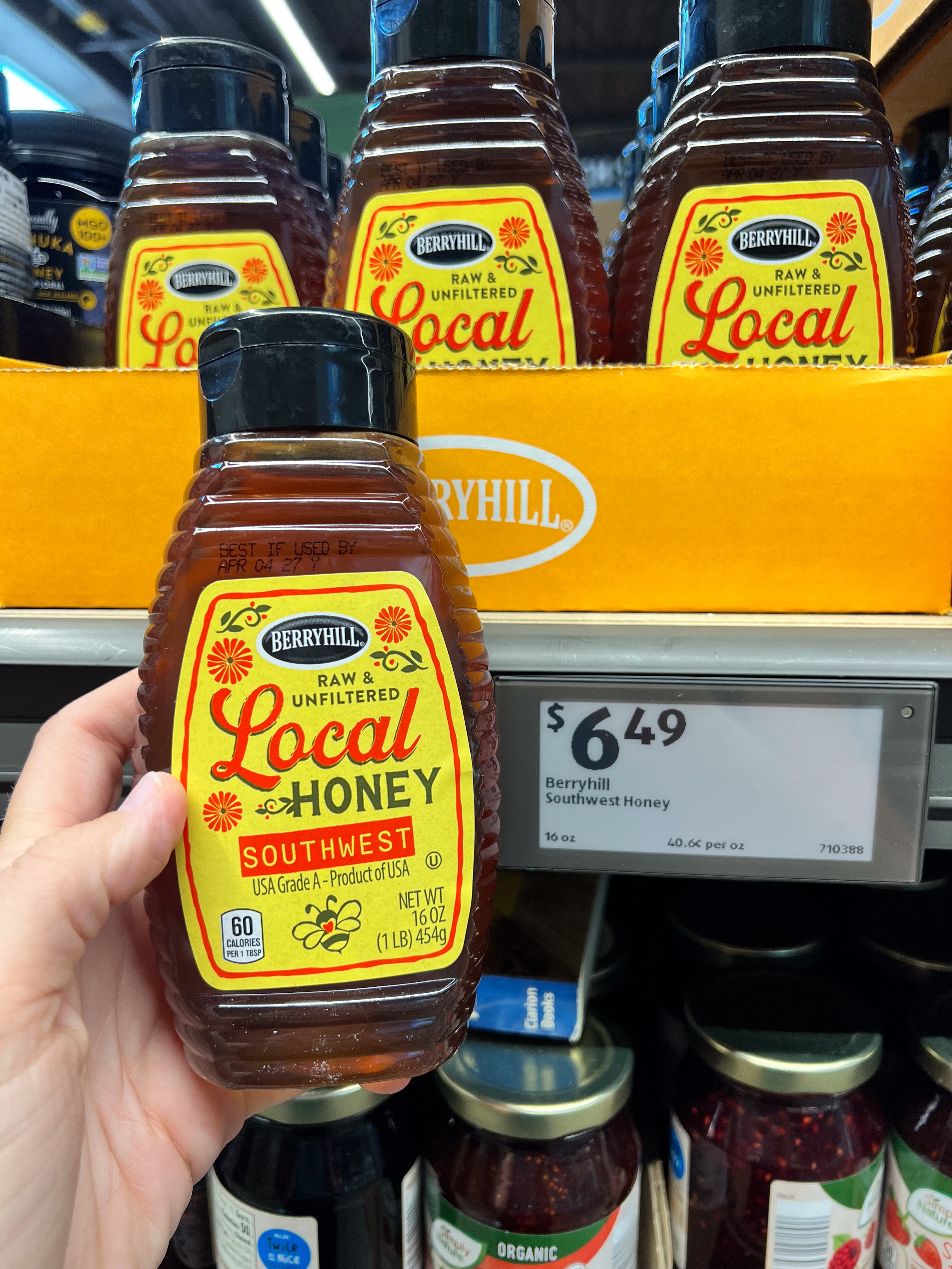 Person holding a bottle of Berryhill Raw Unfiltered Local Southwest Honey, priced at $6.49, displayed on a store shelf