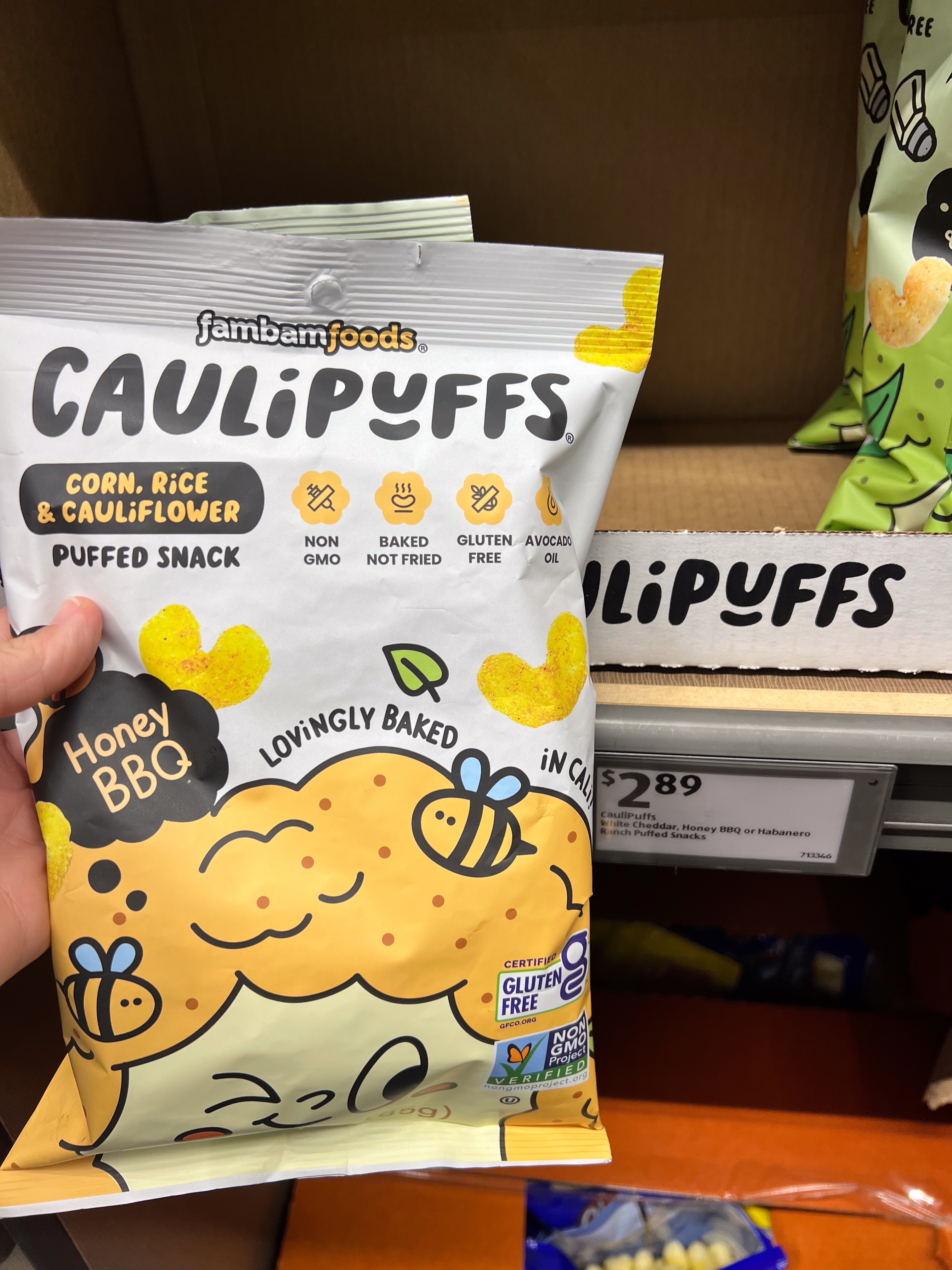 A hand holding a bag of Jamba Foods Caulipuffs, a corn, rice, and cauliflower puffed snack with honey BBQ flavor, gluten-free and non-GMO