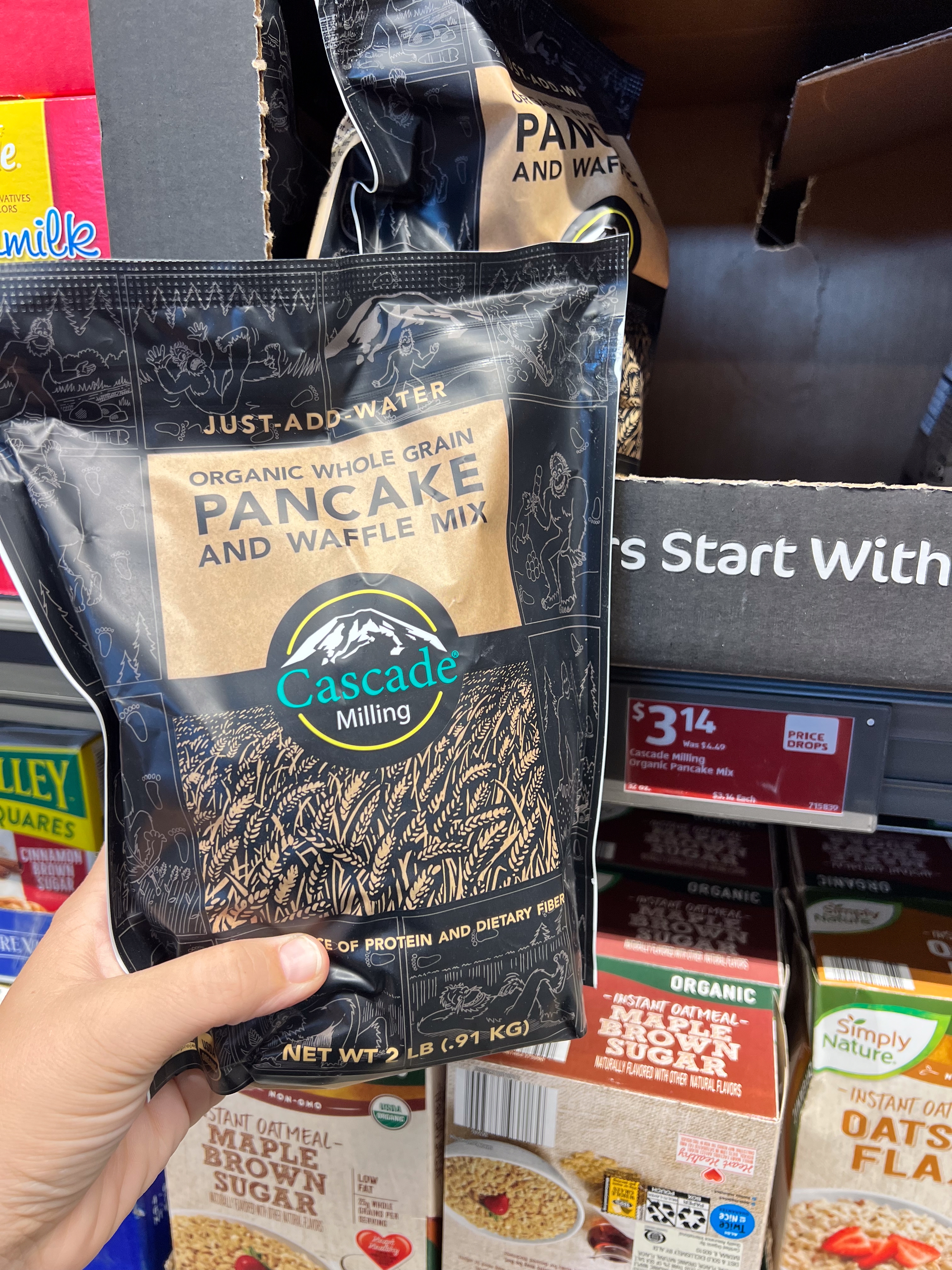 Hand holding a bag of Cascade Milling organic whole grain pancake and waffle mix in a grocery store