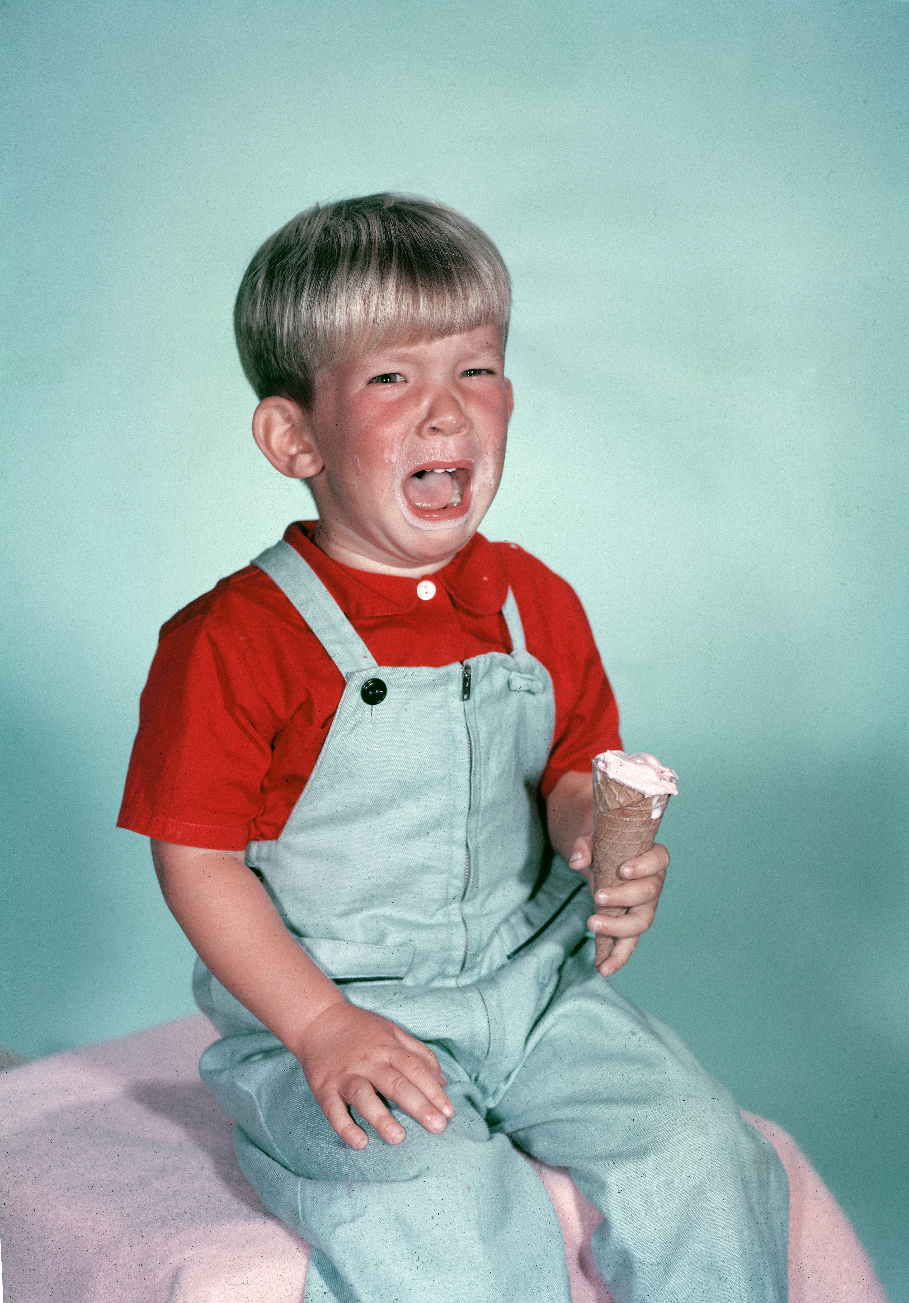Child successful overalls crying portion holding an crystal pick cone, sitting connected a bench