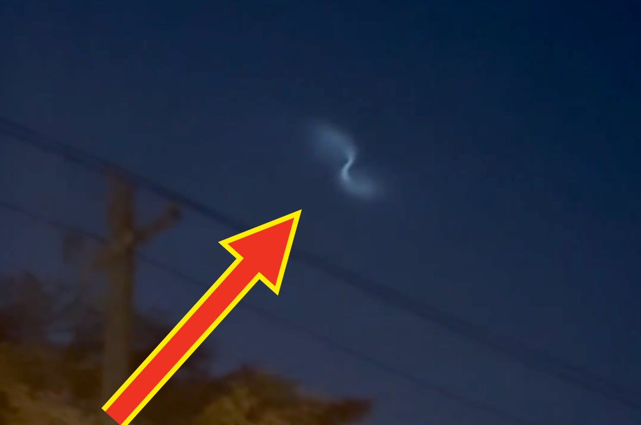 夜空に怪しい光の筋が見える。下には電柱と木がシルエットになっている。