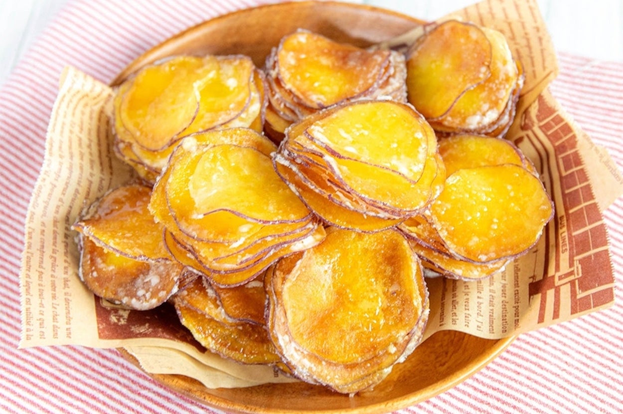 ボウルに山盛りのスライスされたさつまいもチップス、背景に生のさつまいも。