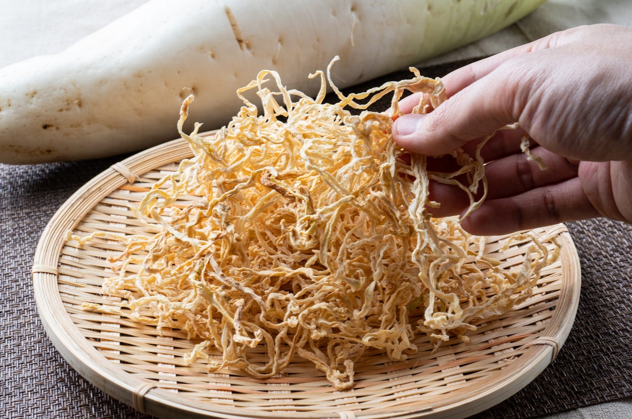 手で持つ切り干し大根の横に大根が置かれた竹ざる。