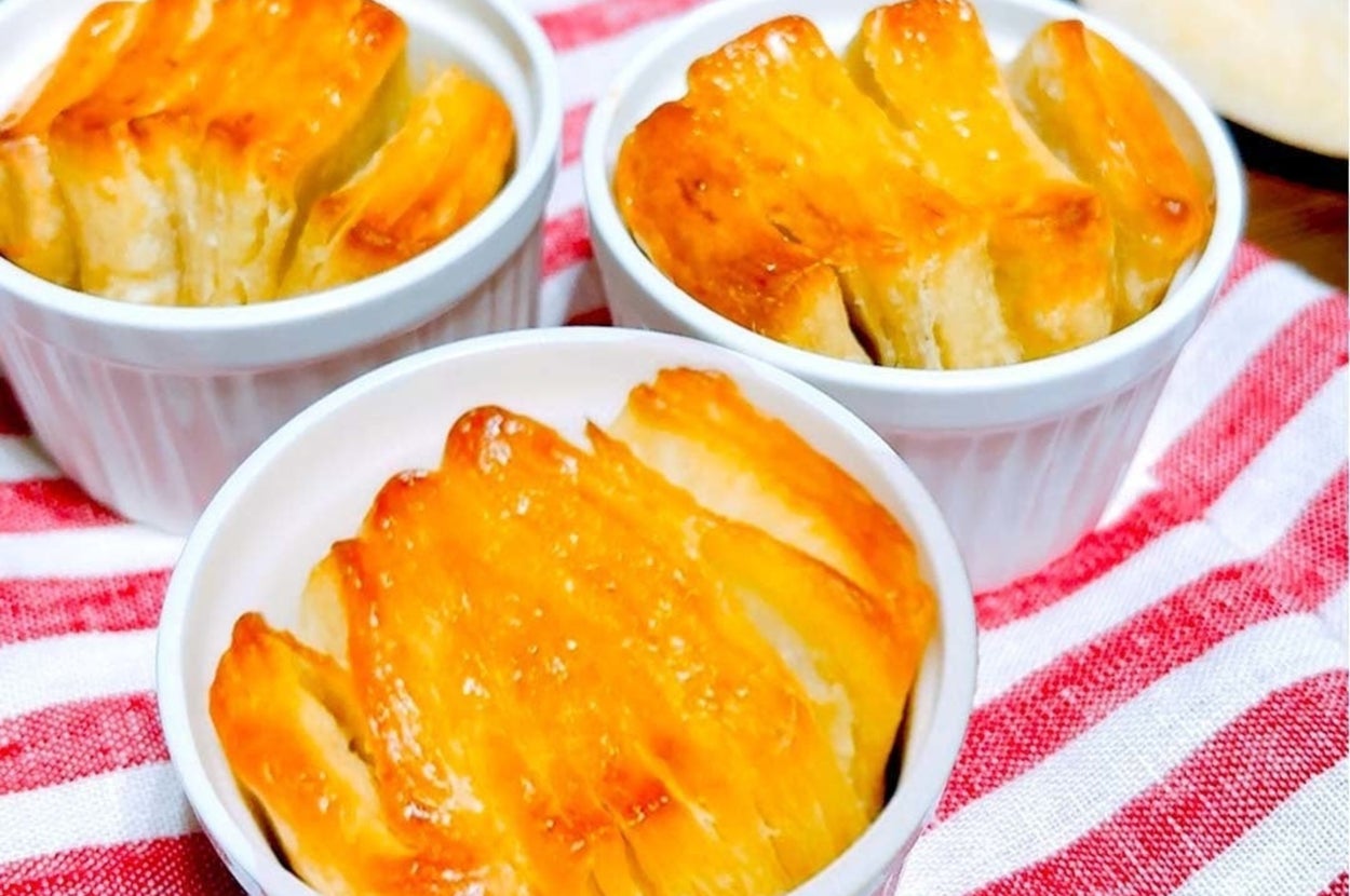 3つの小さな白いココットに焼きたてのペストリーが入っており、後ろにはリンゴが置かれています。