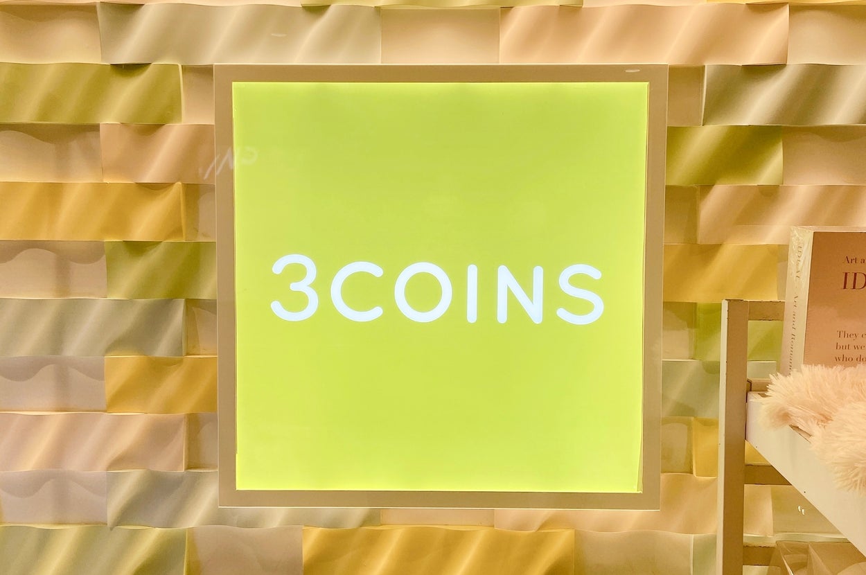 「3COINS」と書かれた看板が、立体的な背景の壁に設置されています。