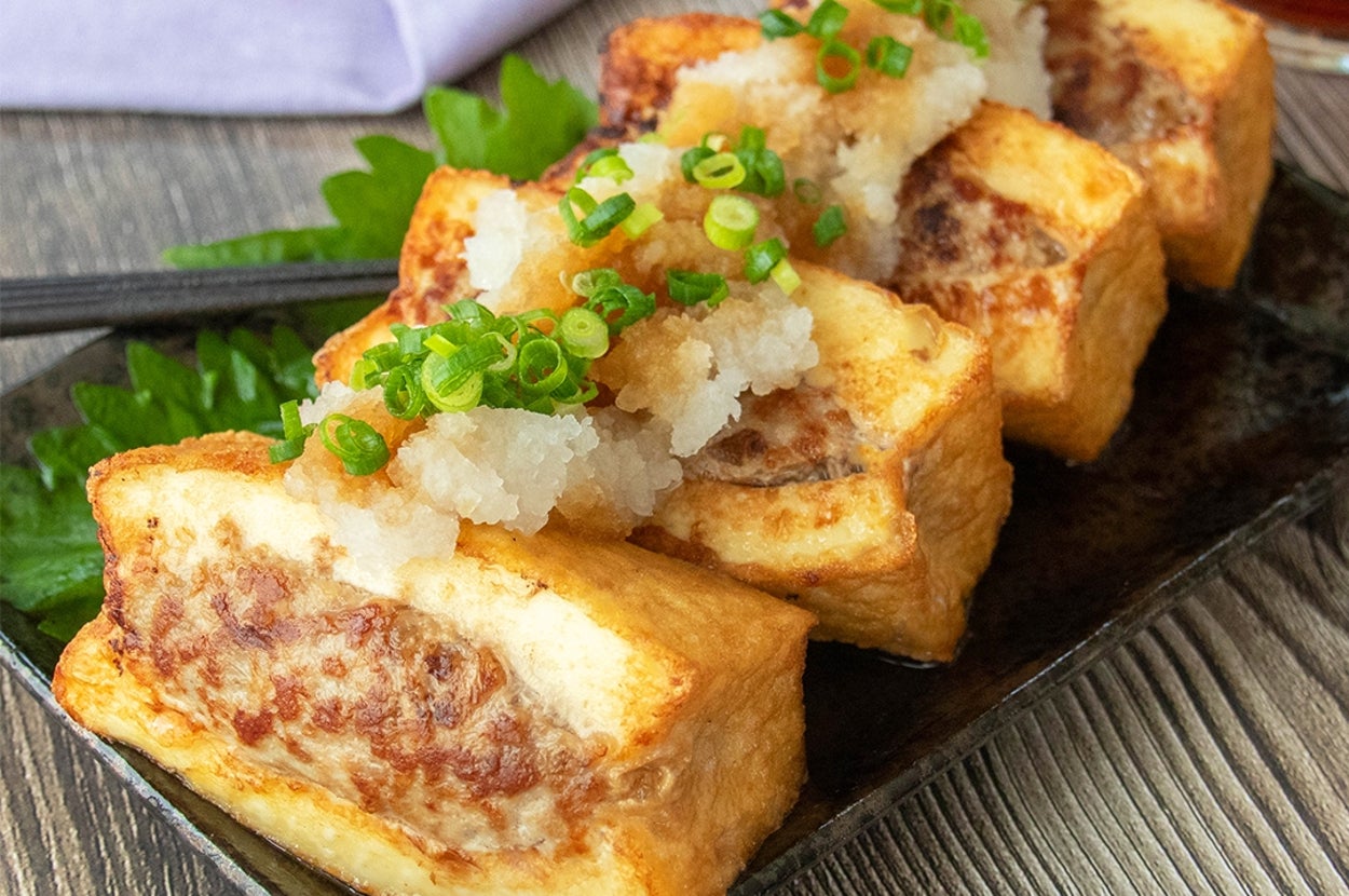 大根おろしと刻みネギがトッピングされた肉詰め厚揚げのおろしポン酢が黒い皿に4つ盛り付けられている。